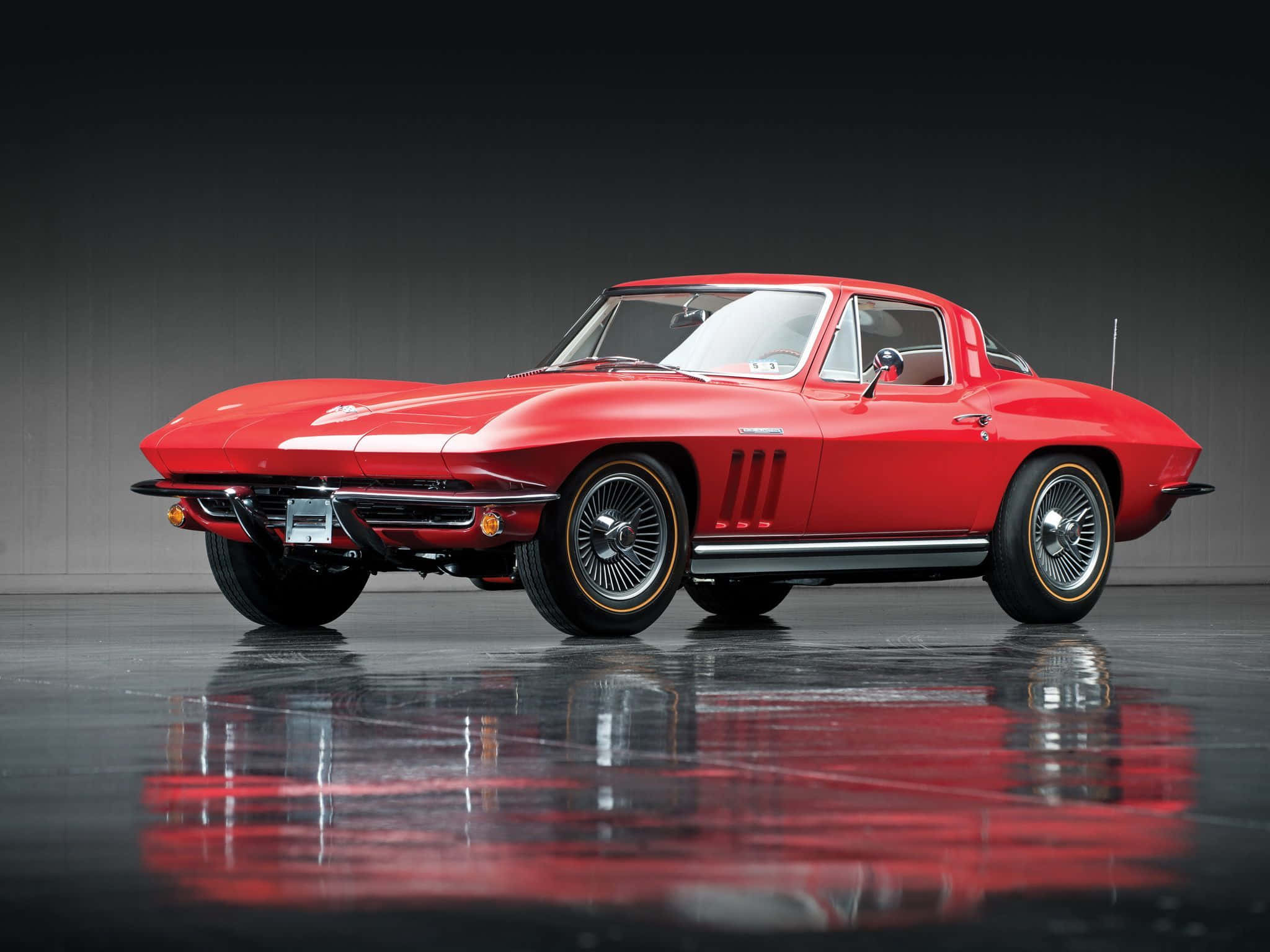 classic 桌布 壁紙 — 一輛光澤的紅色經典Corvette跑車，帶有鍍鉻裝飾和鋼絲輪，在深色工作室背景下完美反射在拋光地板上。