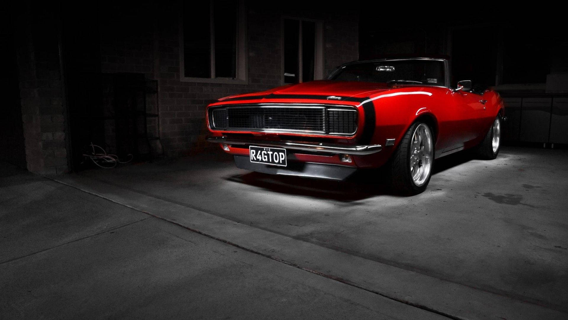 Cool Car 桌布 壁紙 — 一輛光澤的紅色經典敞篷肌肉車在黑暗的車庫中，混凝土地板和磚牆，戲劇性地被照亮。