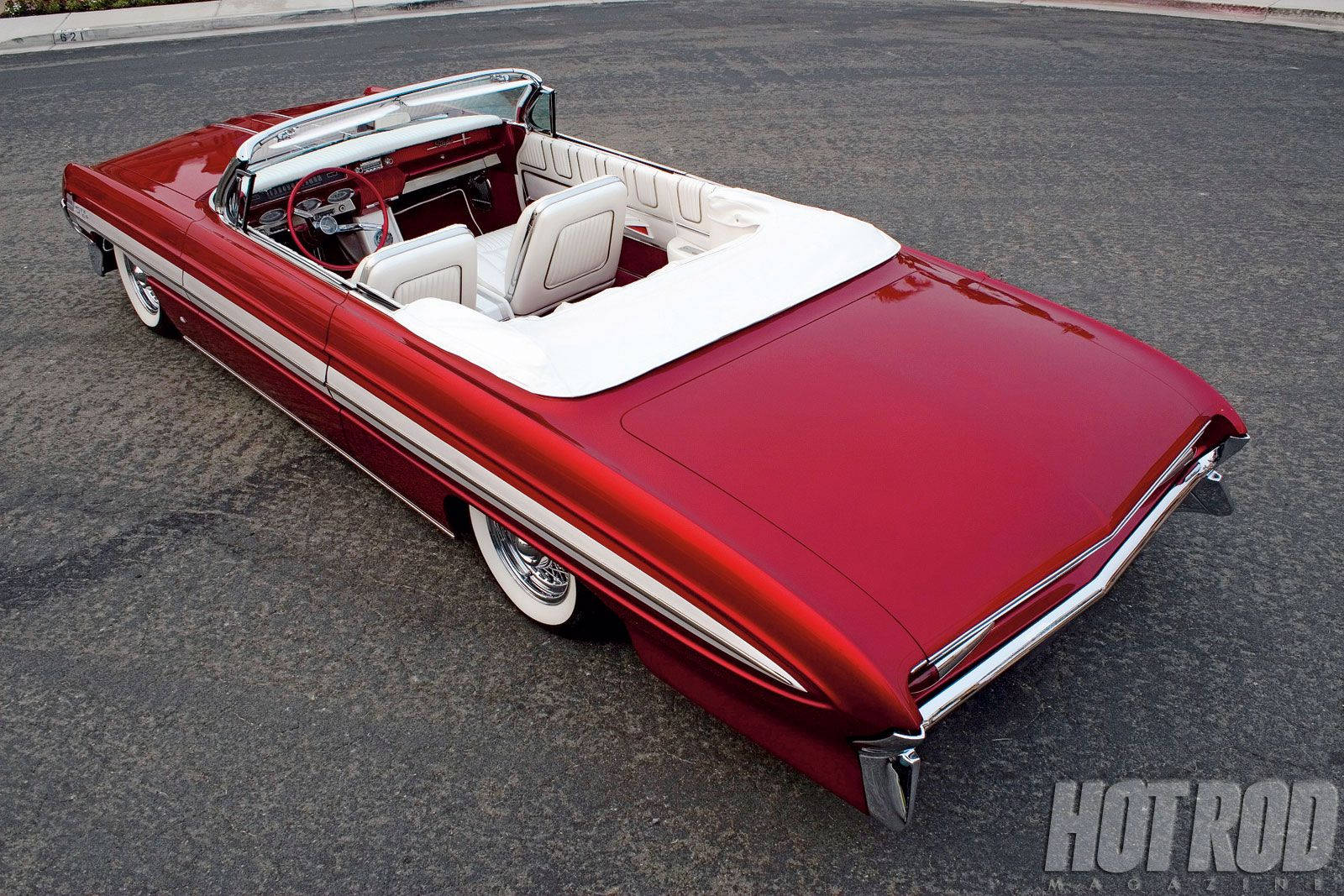 Lowrider 桌布 壁紙 — 一輛光澤的紅色經典敞篷車，配備白色內裝和鍍鉻飾條，停在瀝青路面上，陽光充足。