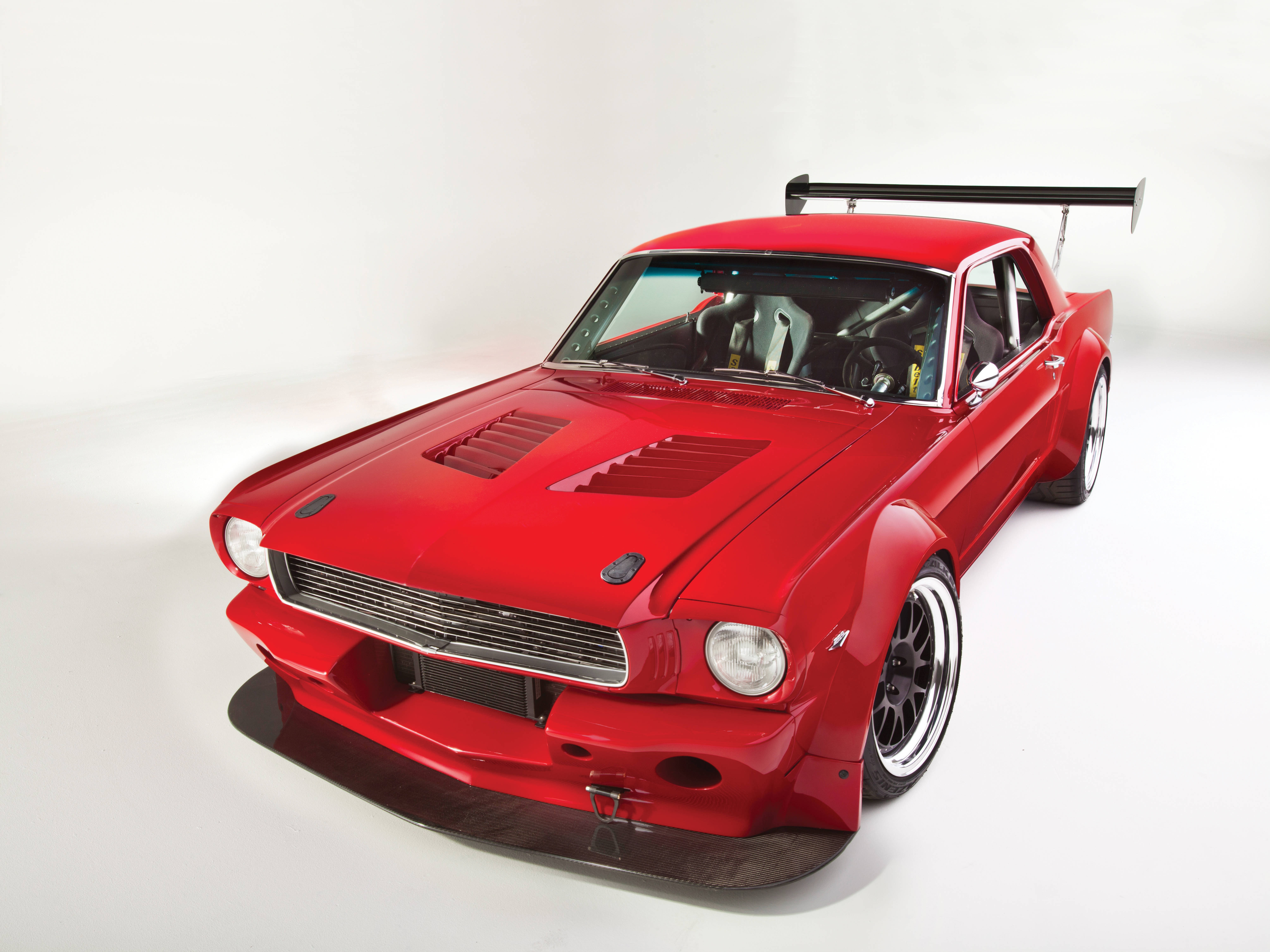 mustang HD 桌布 壁紙 — 一輛光澤的紅色經典肌肉車，帶有大型後翼和定製寬體套件，在純白色工作室背景前擺姿勢。