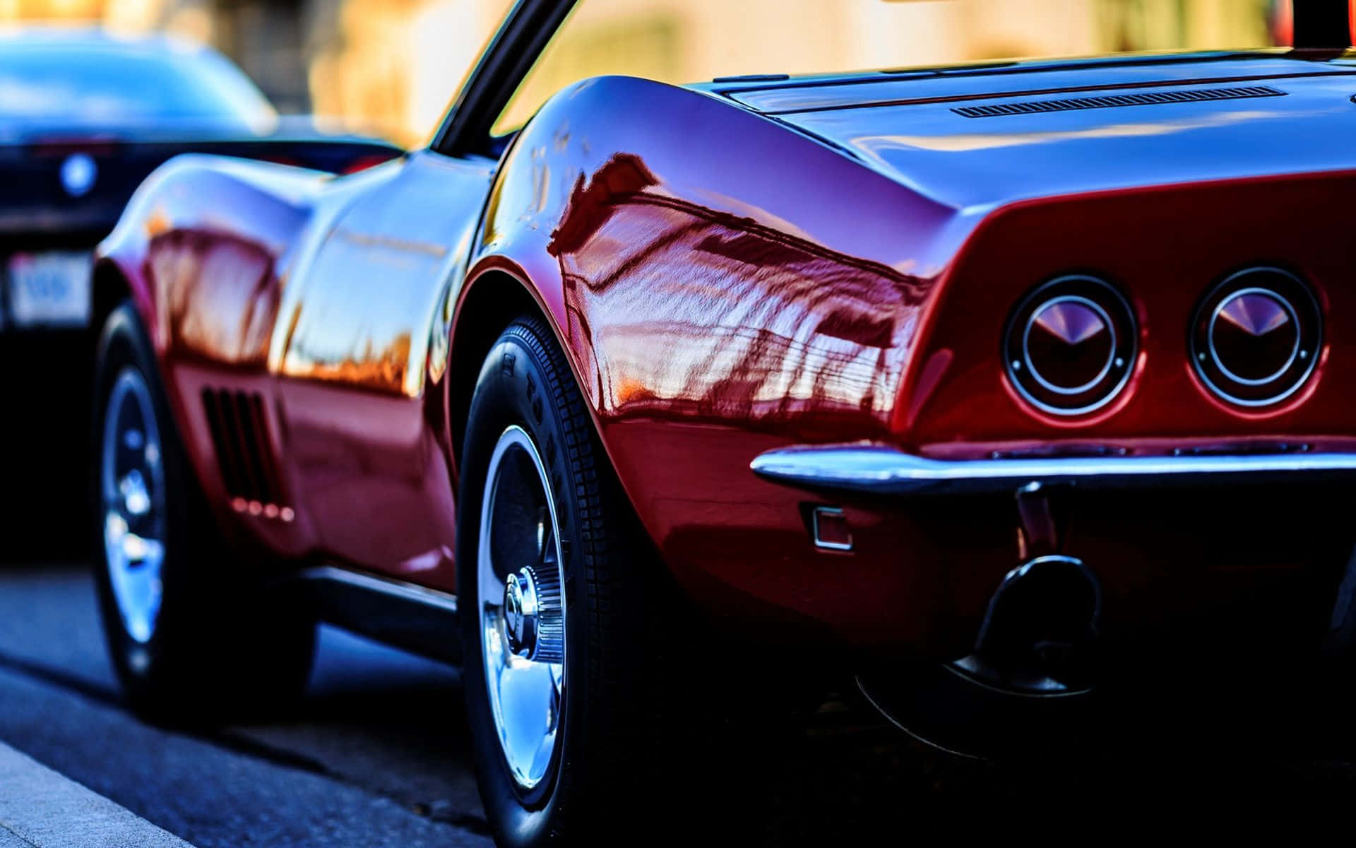 Chevrolet Corvette Stingray 桌布 壁紙 — 一輛光澤的紅色經典肌肉車，帶有鍍鉻細節，在近距離城市鏡頭中反射溫暖的日落。