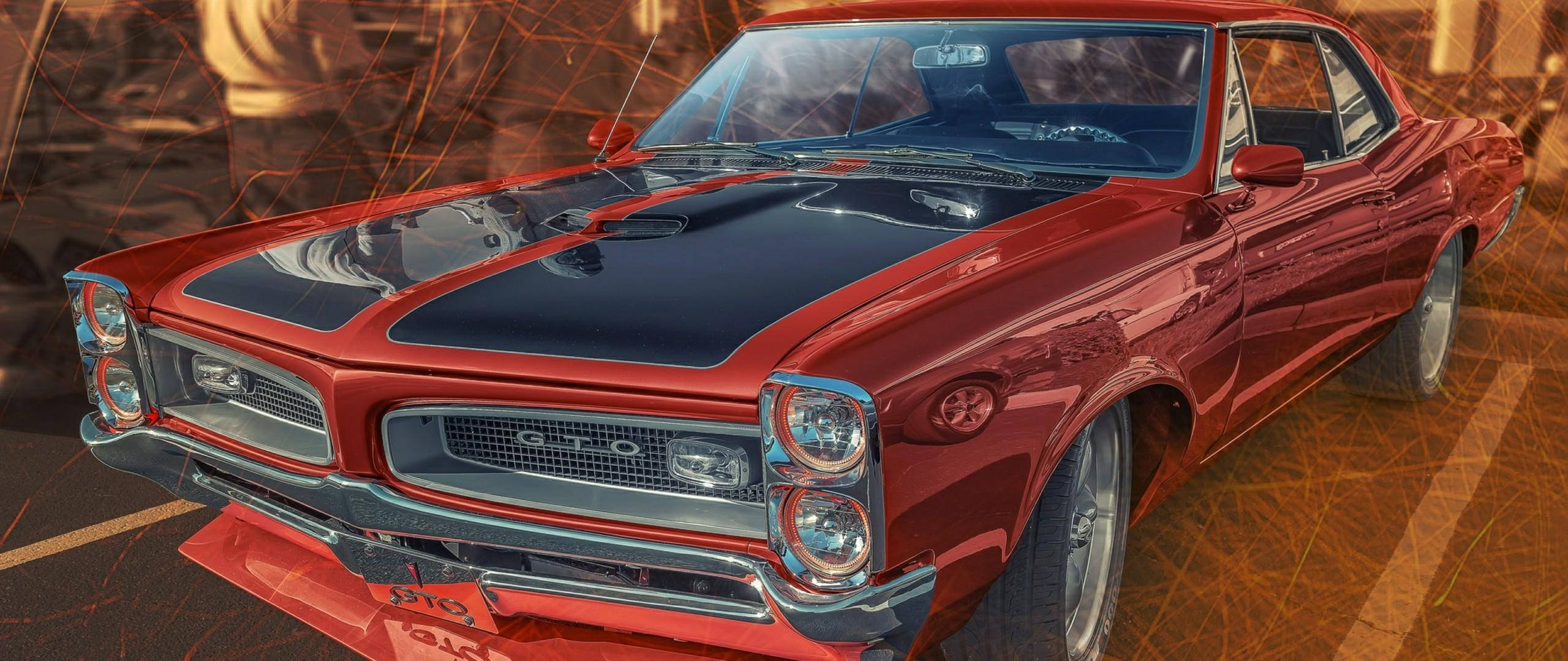 Pontiac 桌布 壁紙 — 一輛光澤的紅色經典肌肉車，帶有黑色引擎蓋條紋，在溫暖的金色燈光下閃耀，背景是火熱的抽象圖案。
