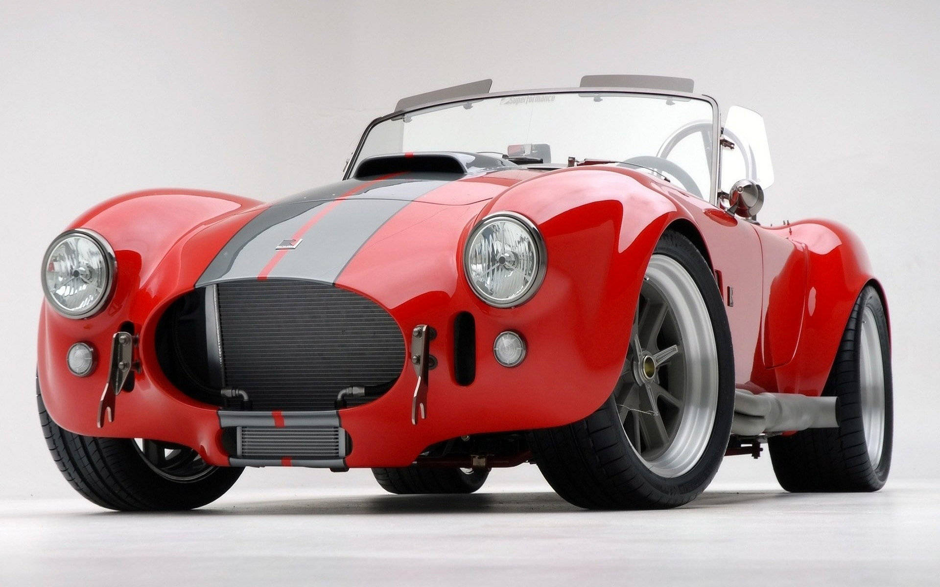 shelby iPhone 桌布 壁紙 — 一輛光澤的紅色經典跑車，帶有黑色賽車條紋和鍍鉻裝飾，在純白色工作室背景前矗立。