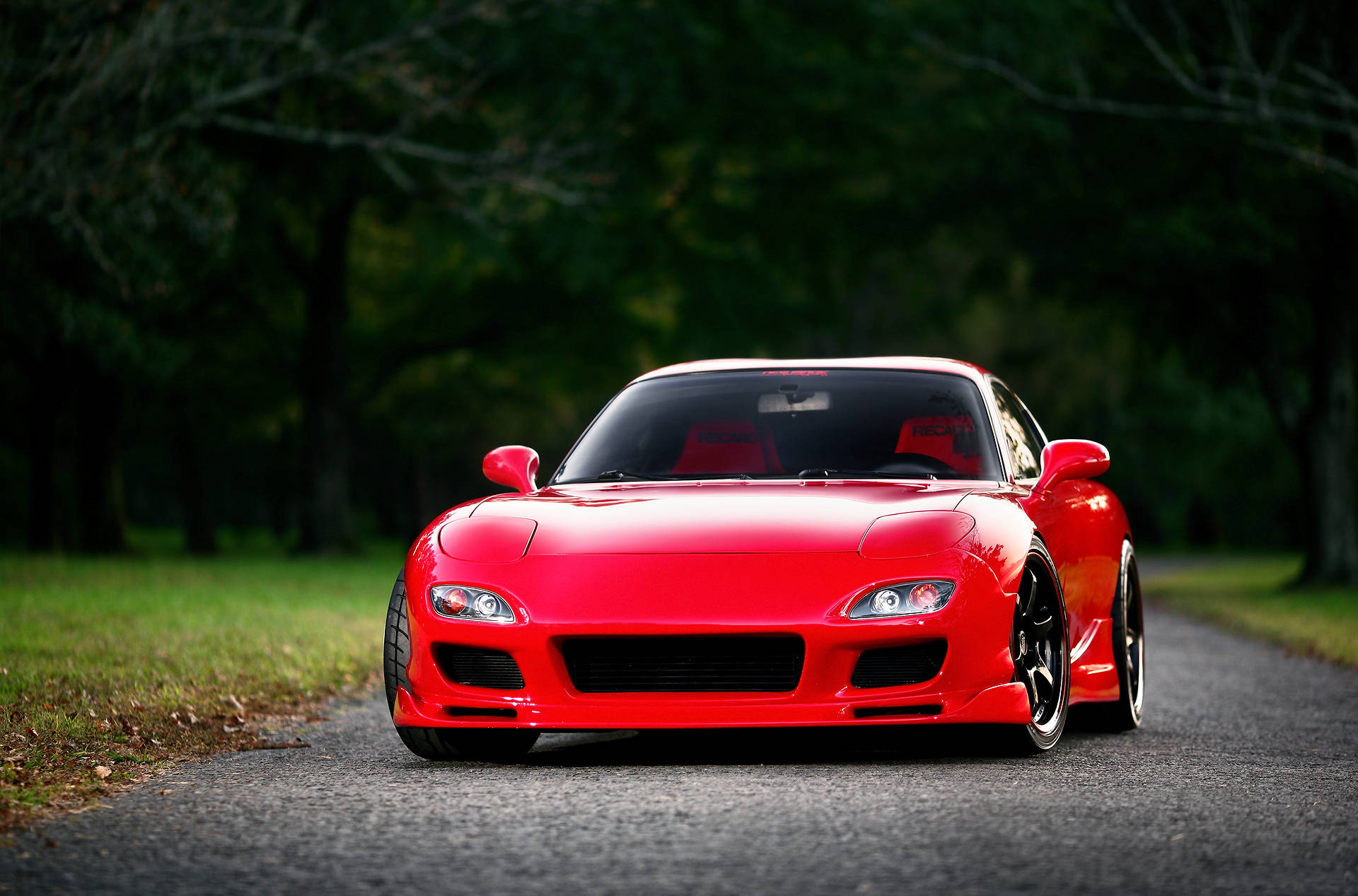 Mazda 桌布 壁紙 — 一輛光澤的紅色跑車搭配黑色輪圈，在柔和自然光下停在兩旁樹木的柏油路中央。