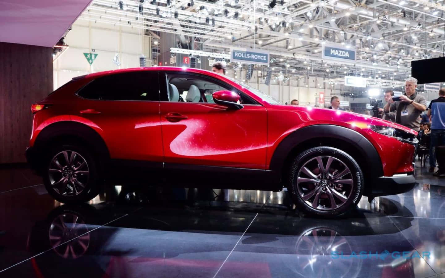 Mazda Cx-30 桌布 壁紙 — 一輛光澤的紅色馬自達CX-30 SUV在車展的反射地板上，在明亮的展覽燈光下閃閃發光。