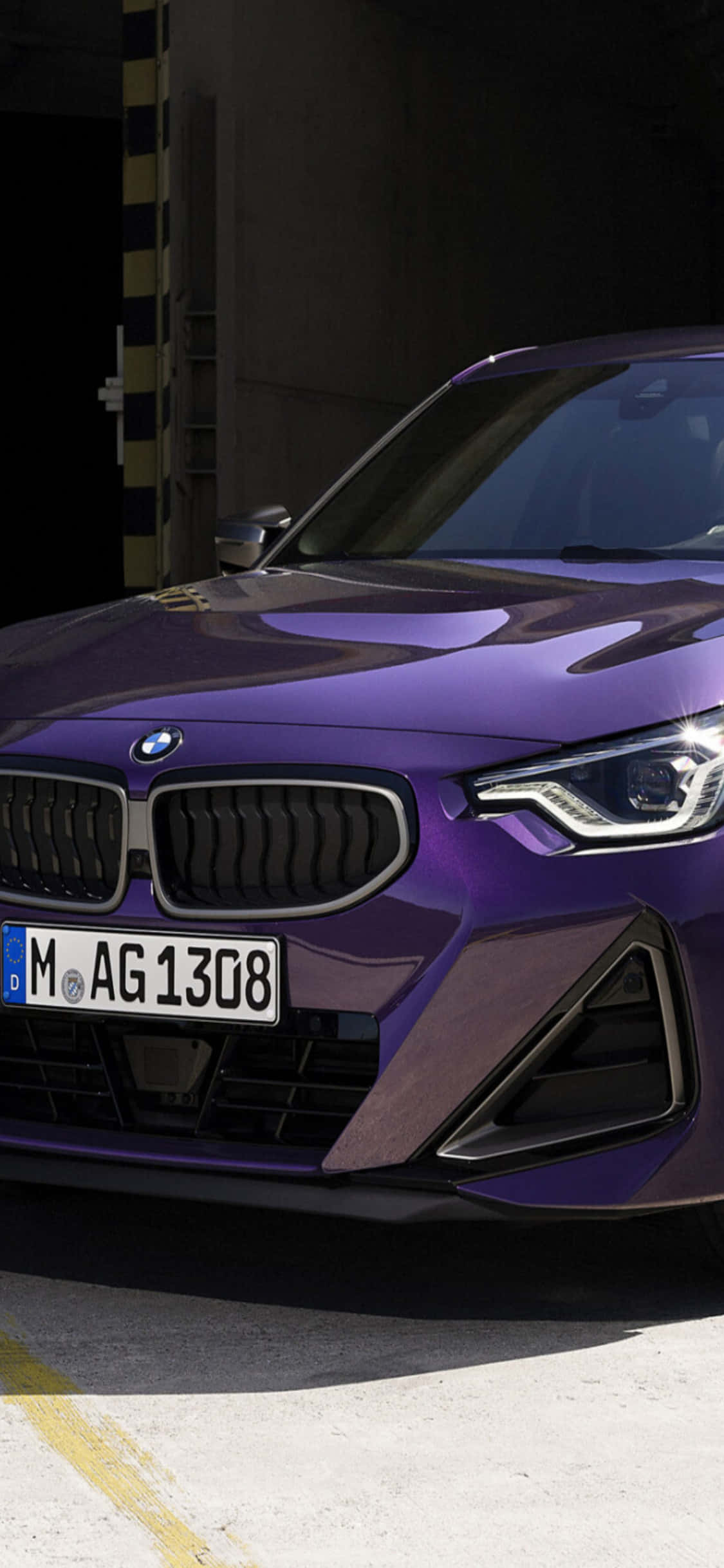 iPhone X Bmw 桌布 壁紙 — 一輛光澤的紫色BMW跑車停放在車庫中，戲劇性的燈光凸顯其流線型的前臉設計。