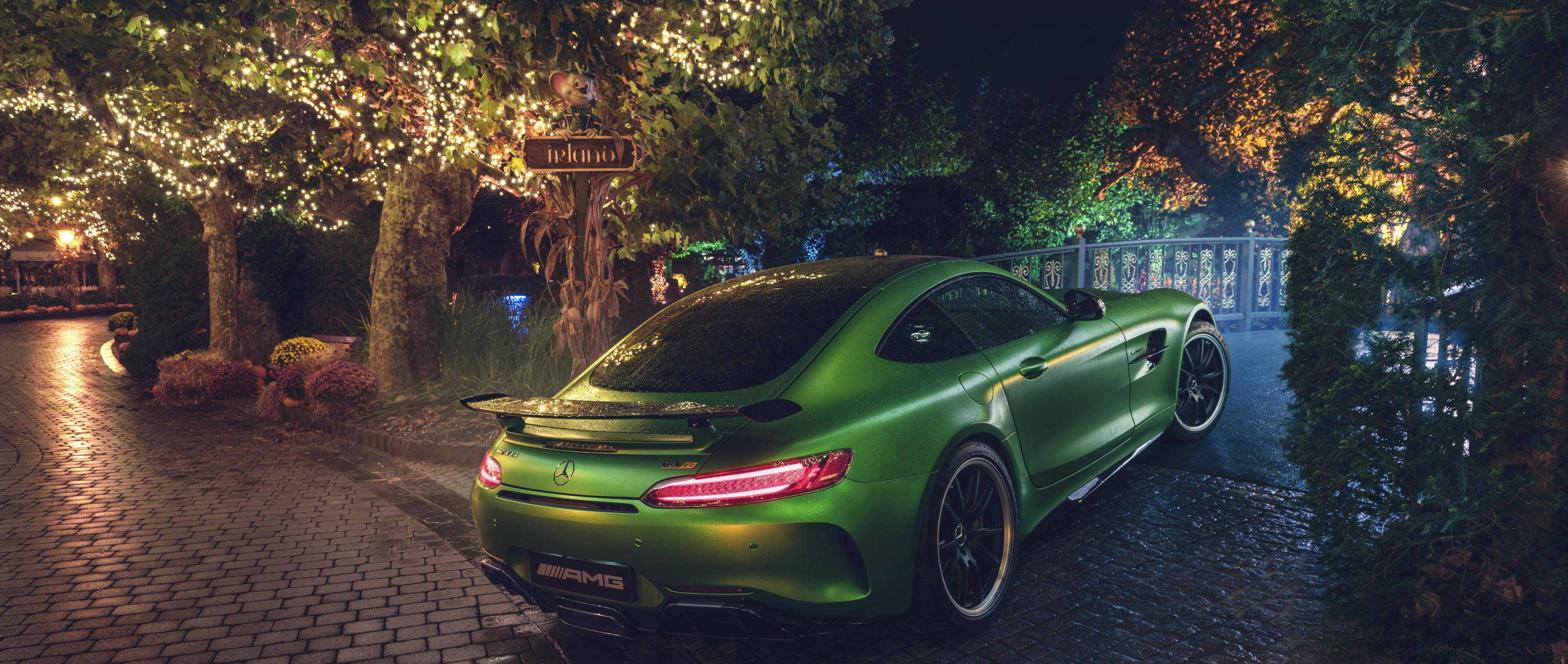 Gtr 桌布 壁紙 — 一輛光澤的綠色AMG跑車在夜晚濕漉漉的鵝卵石小徑上，在串燈下閃耀。