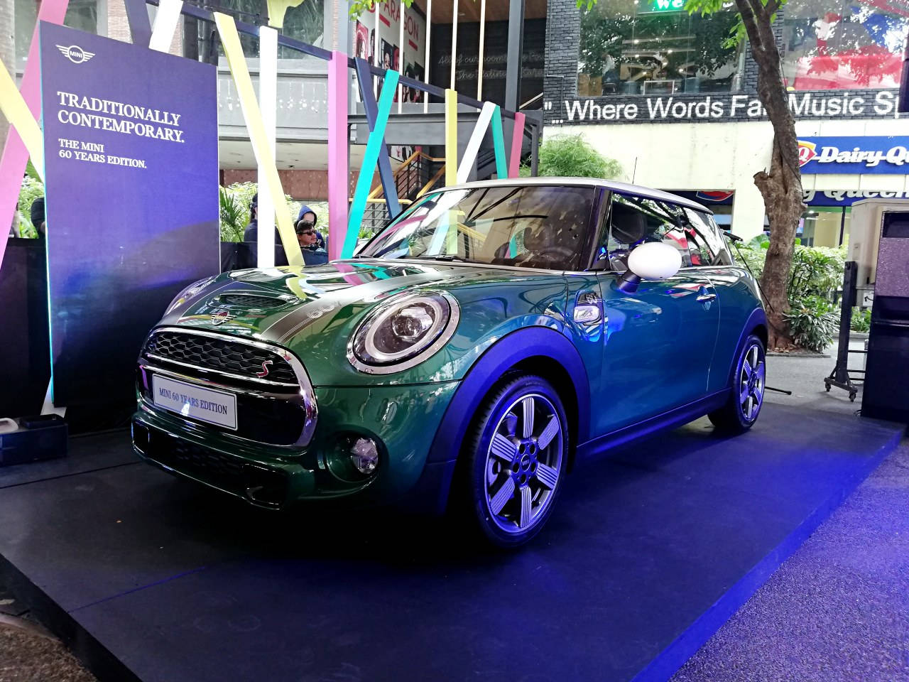 Mini 桌布 壁紙 — 一輛光澤的綠色MINI Cooper S 60 Years Edition汽車在充滿活力的藍色舞台燈光下，於城市戶外發布活動中閃閃發光。
