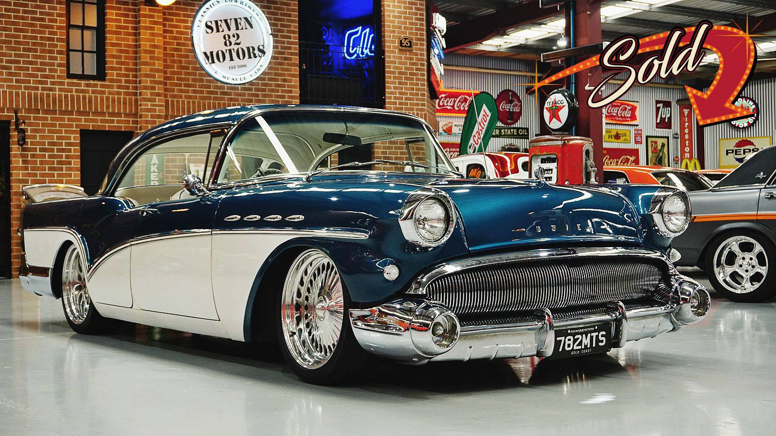 Buick 桌布 壁紙 — 一輛光澤的藍白經典汽車在充滿復古標誌的復古車庫中，在明亮的燈光下閃閃發光。