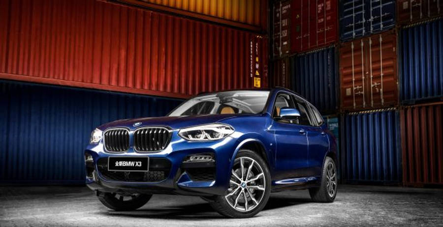 桌布 壁紙 — 一輛光澤的藍色BMW X3 SUV停在堆疊的貨運集裝箱前，光線效果戲劇化。
