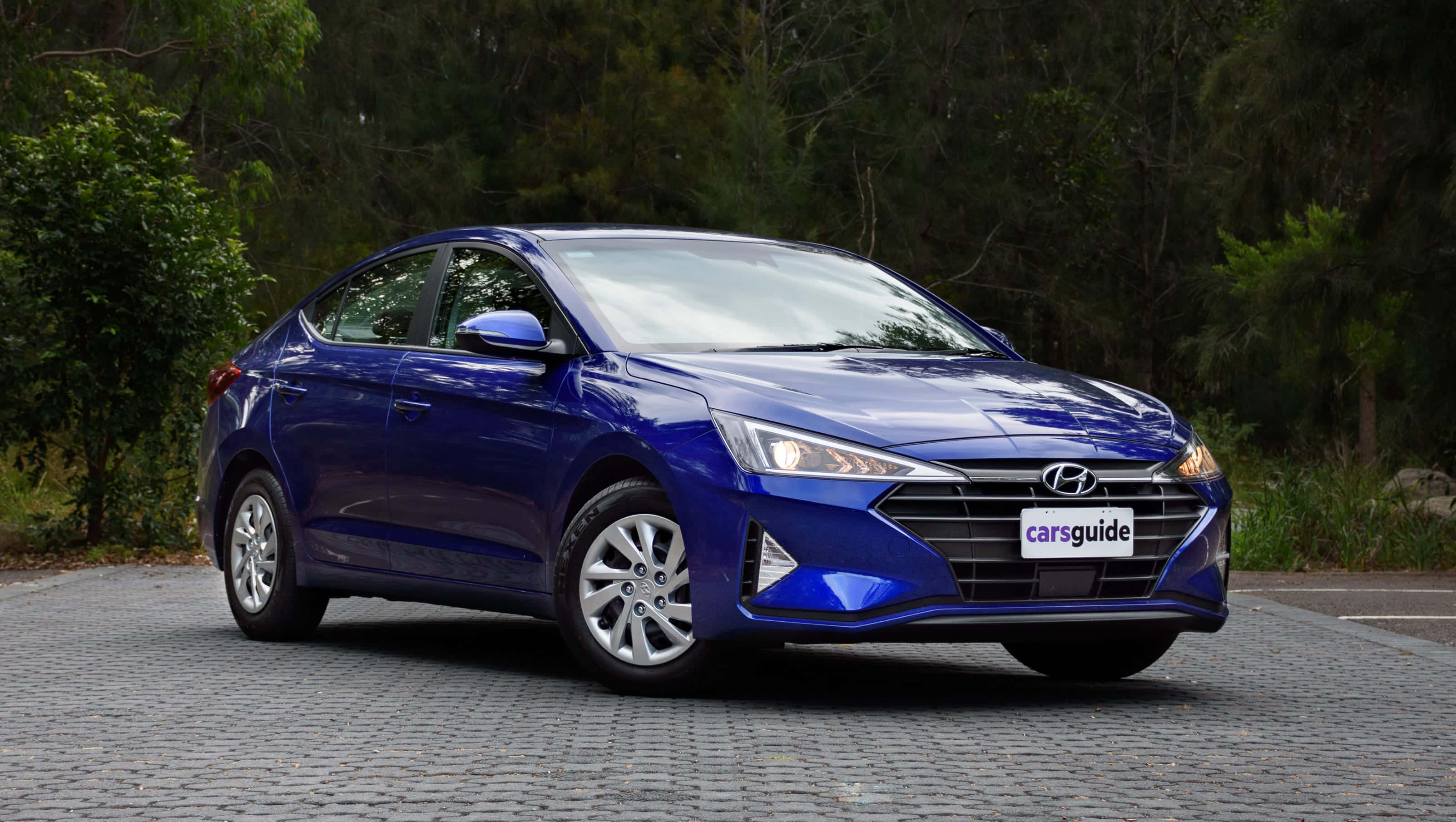 Hyundai 桌布 壁紙 — 一輛光澤的藍色現代轎車停在鵝卵石路面上，背景是茂密的綠色樹木。