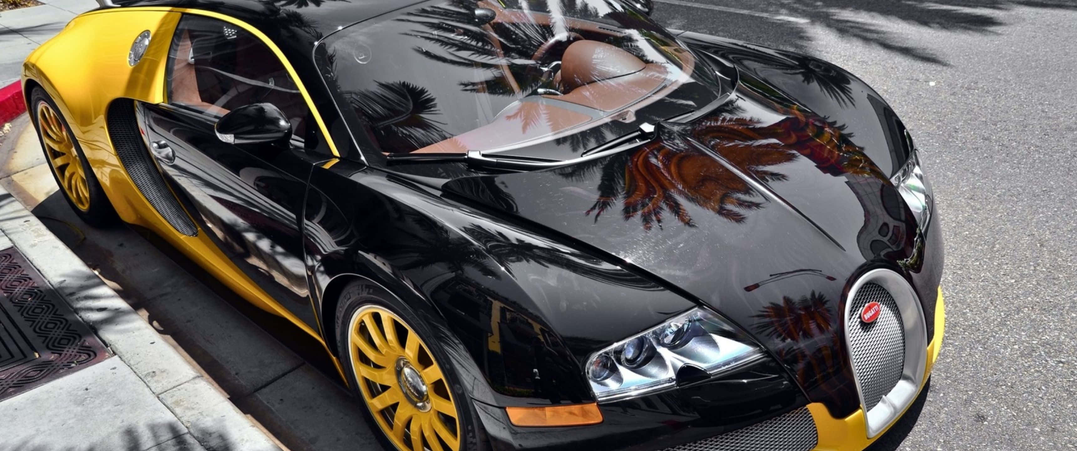 3440x1440p Bugatti 桌布 壁紙 — 一輛光澤的黑色和黃色Bugatti Veyron停放在陽光明媚的街道上，拋光的引擎蓋反射出棕櫚樹。