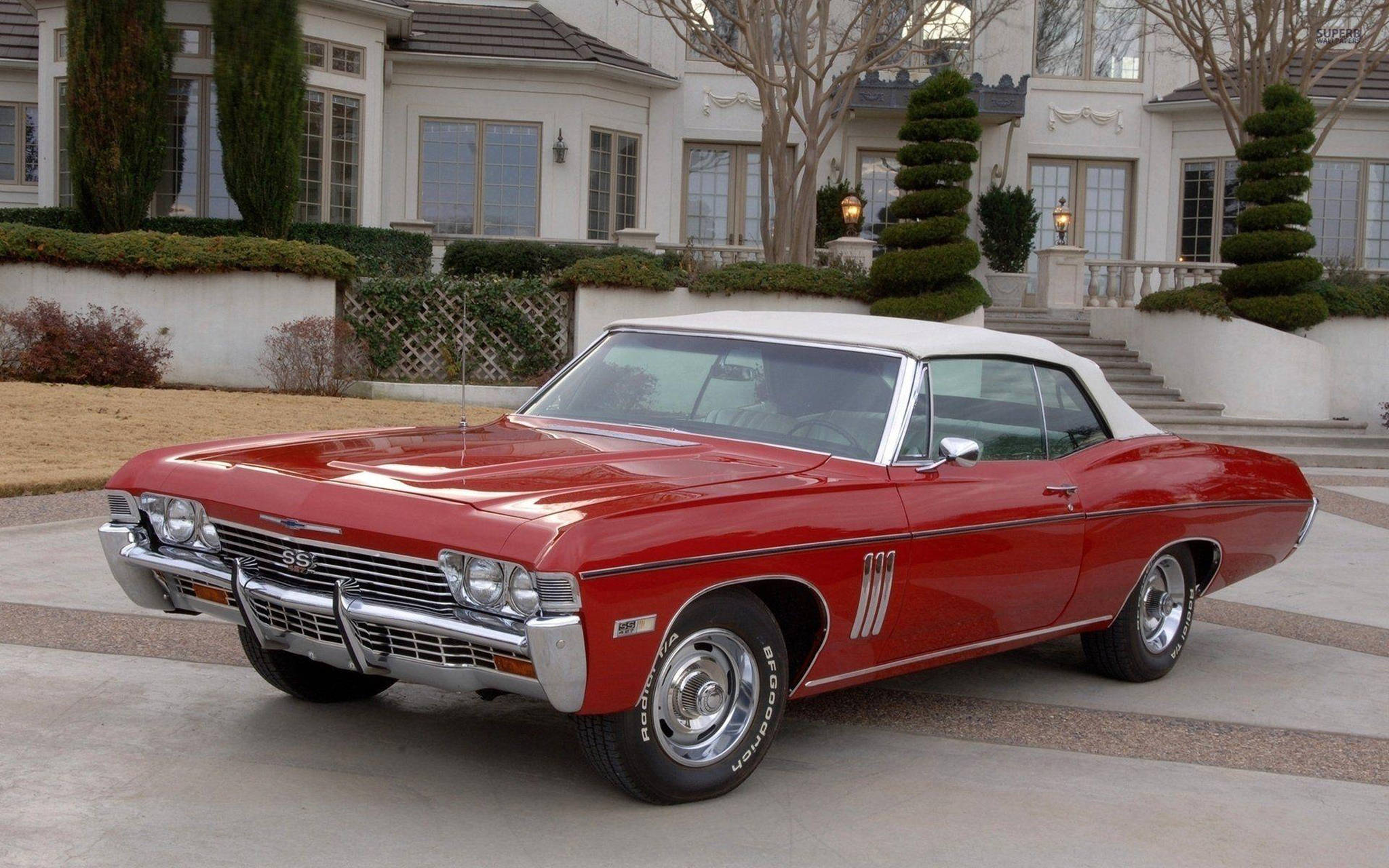 chevrolet impala 1967 桌布 壁紙 — 一輛光澤紅色1967年雪佛蘭Chevelle SS敞篷車，白色車頂，停泊在豪華豪宅前的瓷磚車道上。