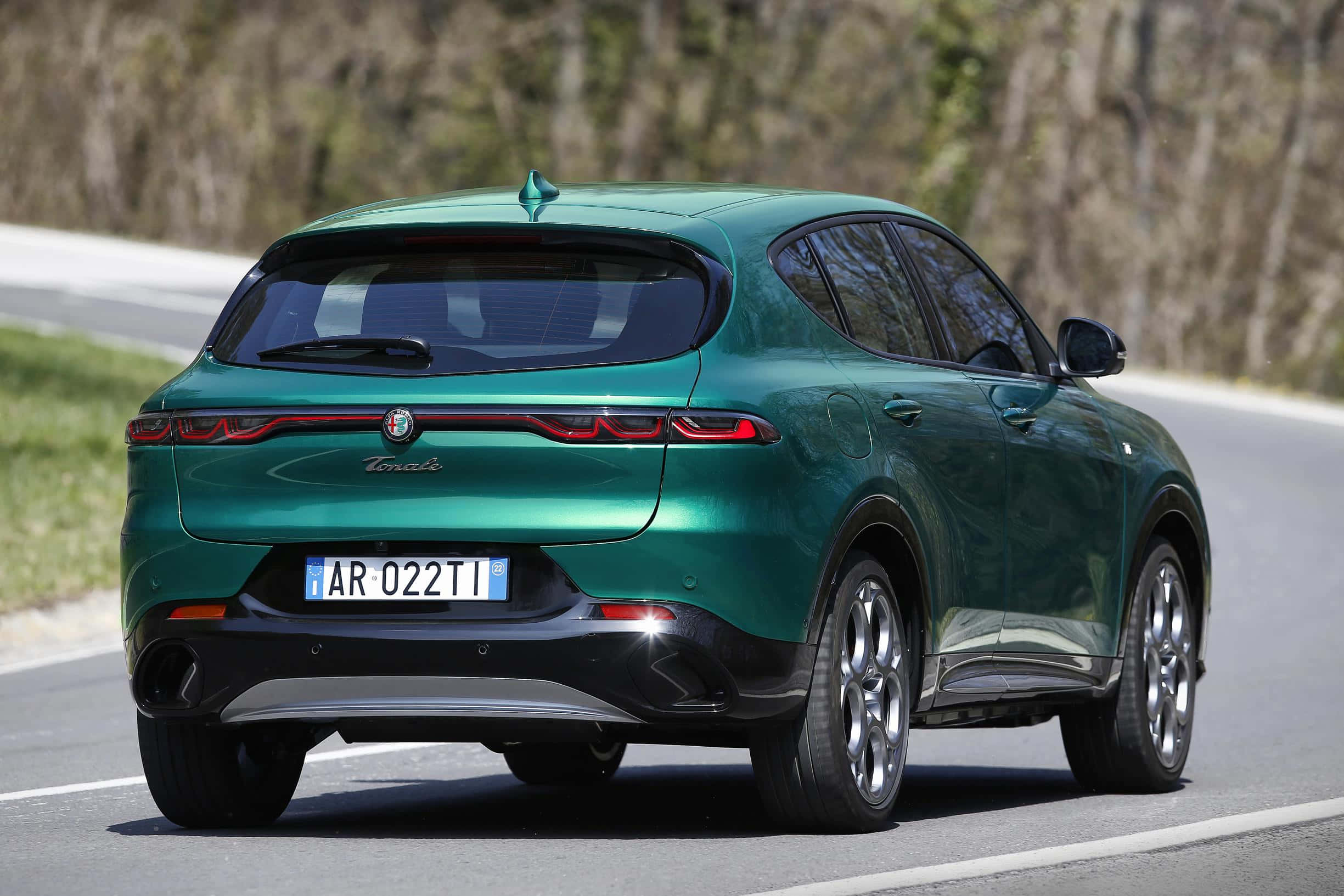 愛快羅密歐 桌布 壁紙 — 一輛光澤綠色的Alfa Romeo Tonale SUV在晴朗的日子沿著蜿蜒道路穿過樹林地區行駛。