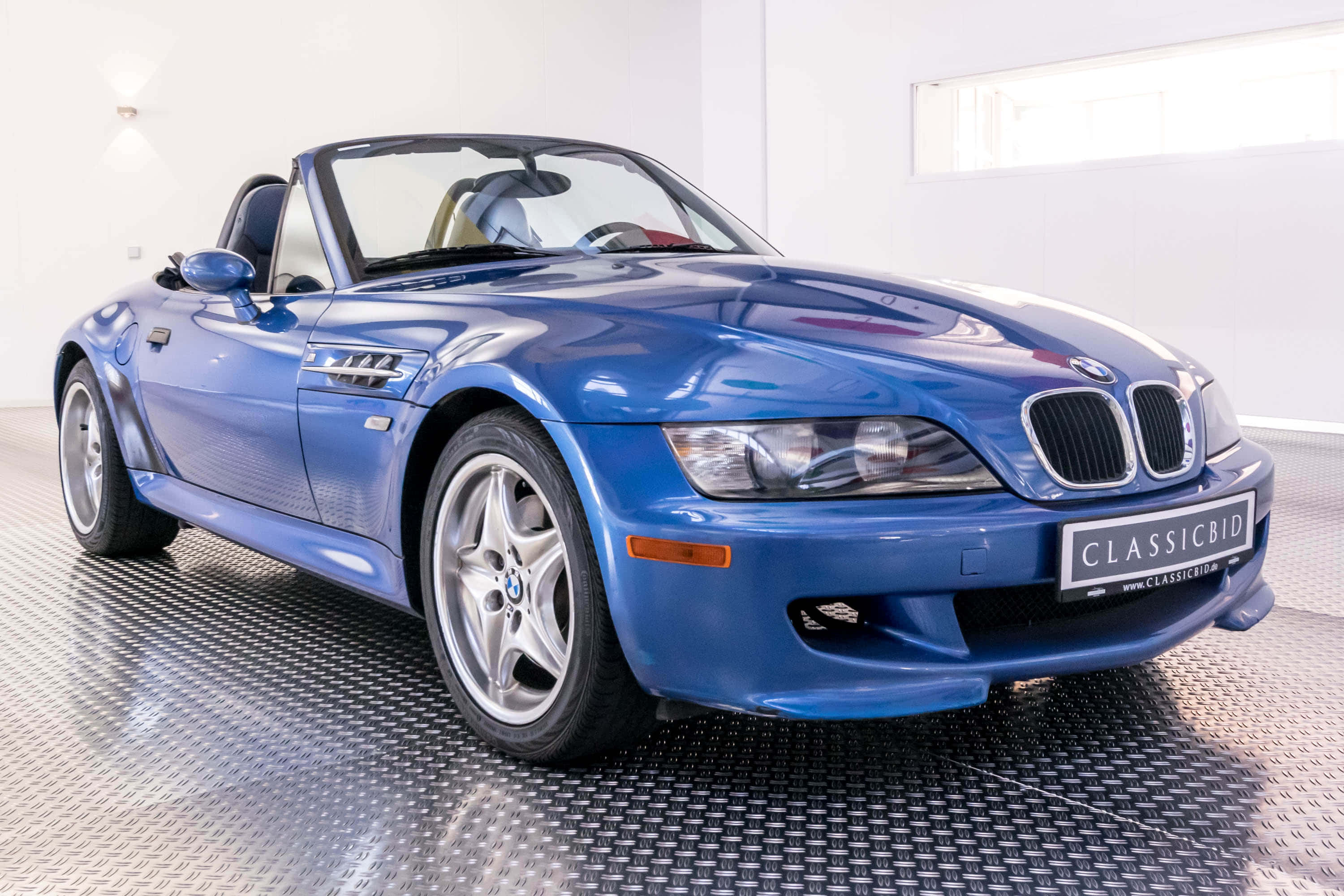 Bmw Z3 桌布 壁紙 — 一輛光澤藍色BMW Z3敞篷跑車在簡約白色車庫的鑽石紋地板上，在明亮燈光下閃閃發光。