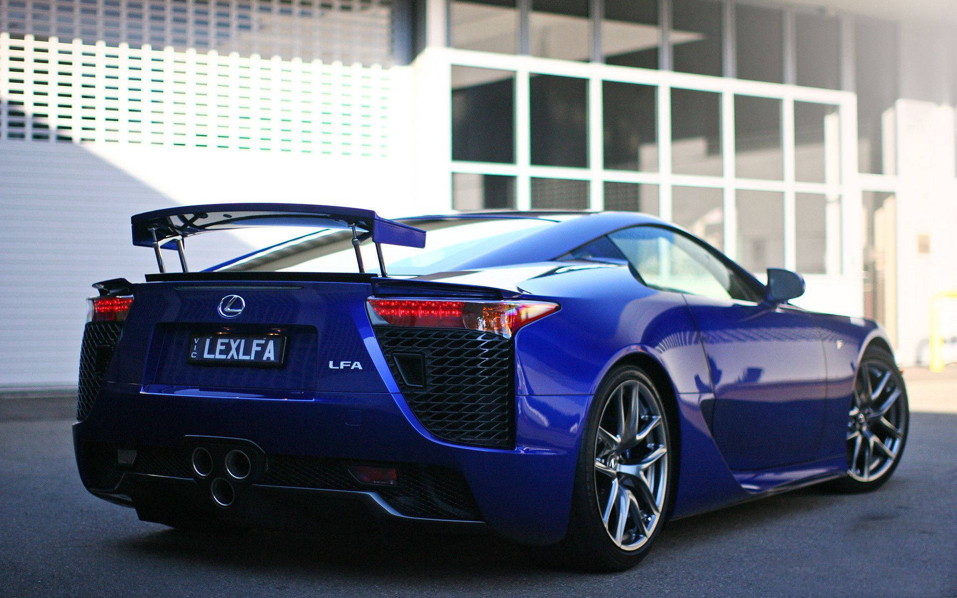 Lexus 桌布 壁紙 — 一輛光澤藍色Lexus LFA跑車停在一棟現代玻璃建築前，陽光在其曲線上反射。