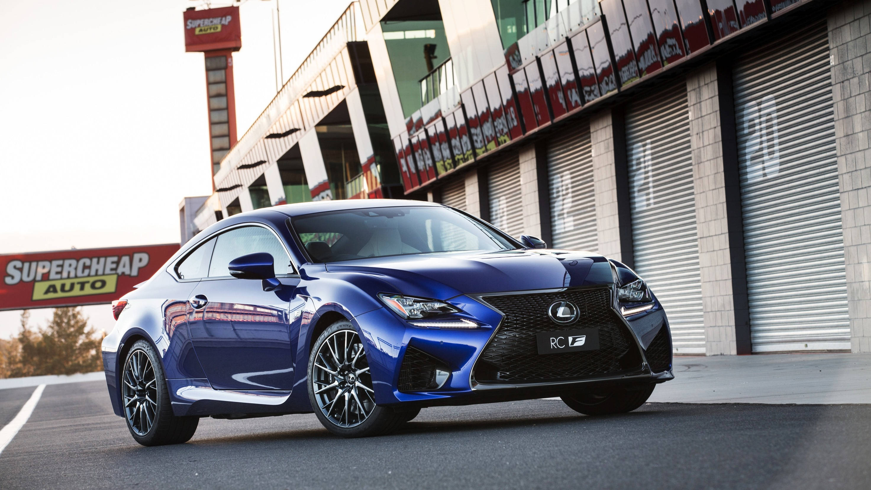 凌志 桌布 壁紙 — 一輛光澤藍色Lexus RC F跑車停放在賽車場車庫前，帶有'Supercheap Auto'標誌。
