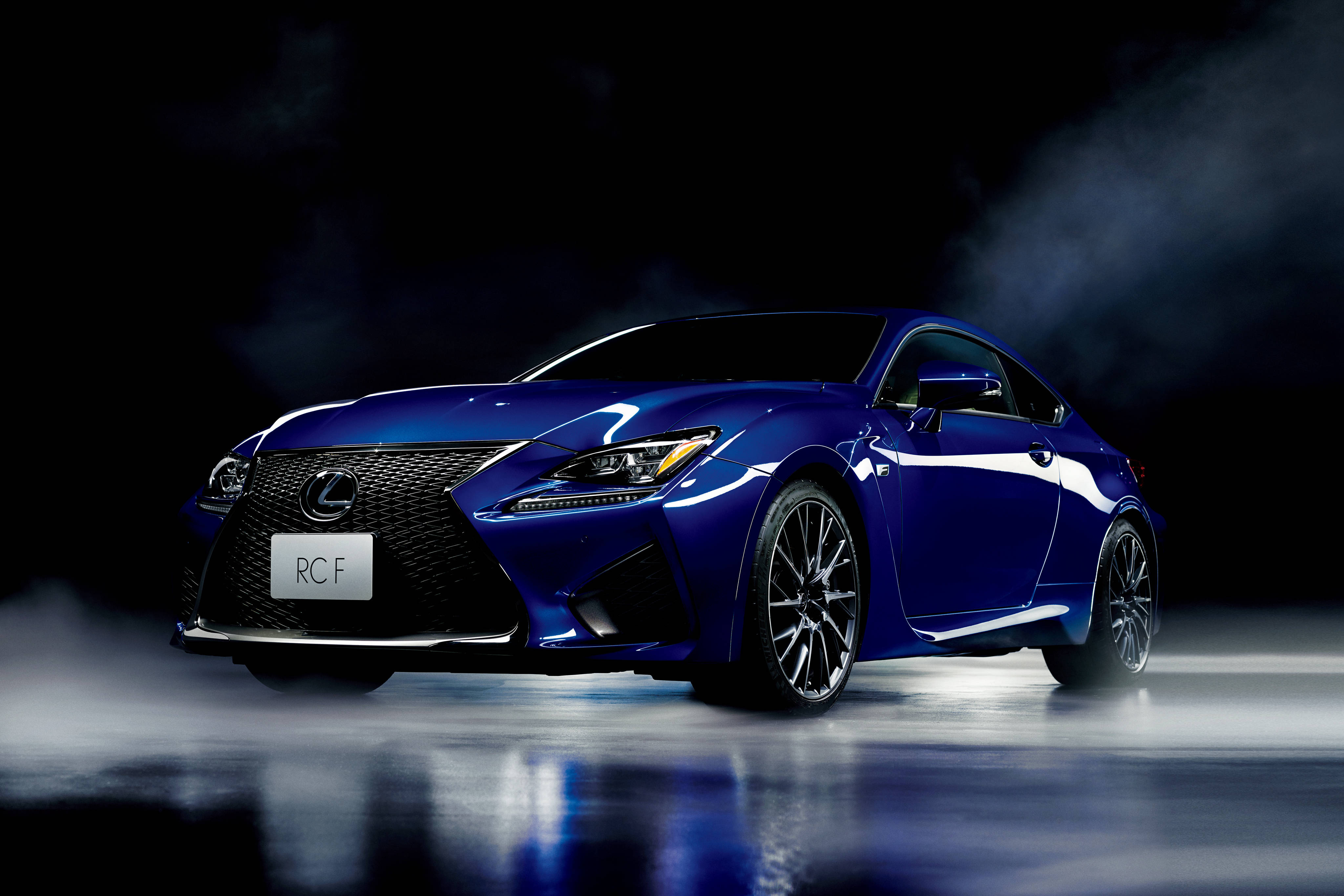 lexus iPhone 桌布 壁紙 — 一輛光澤藍色Lexus RCF跑車在攝影棚燈光下閃耀，煙霧在其流線型車身周圍旋繞，映照在反光地板上。