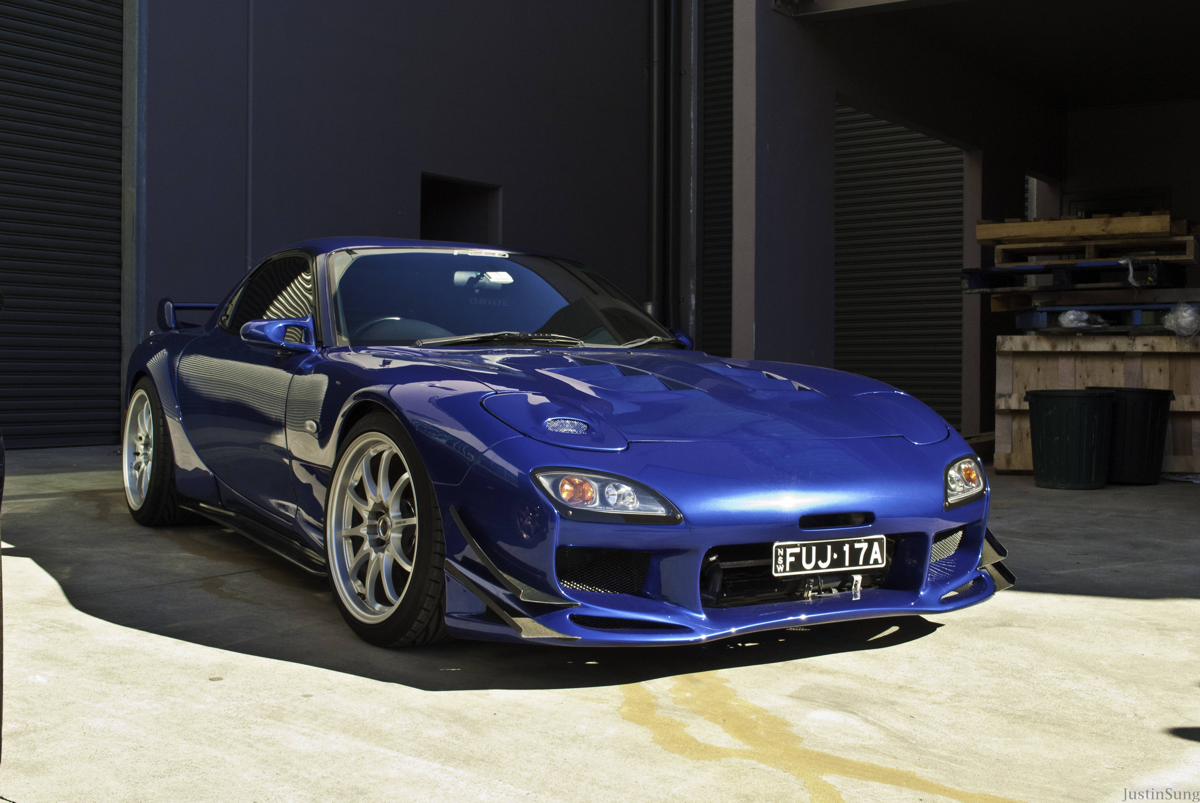 Mazda 桌布 壁紙 — 一輛光澤藍色Mazda RX-7跑車停放在車庫中，陽光在混凝土上投射出銳利的陰影。