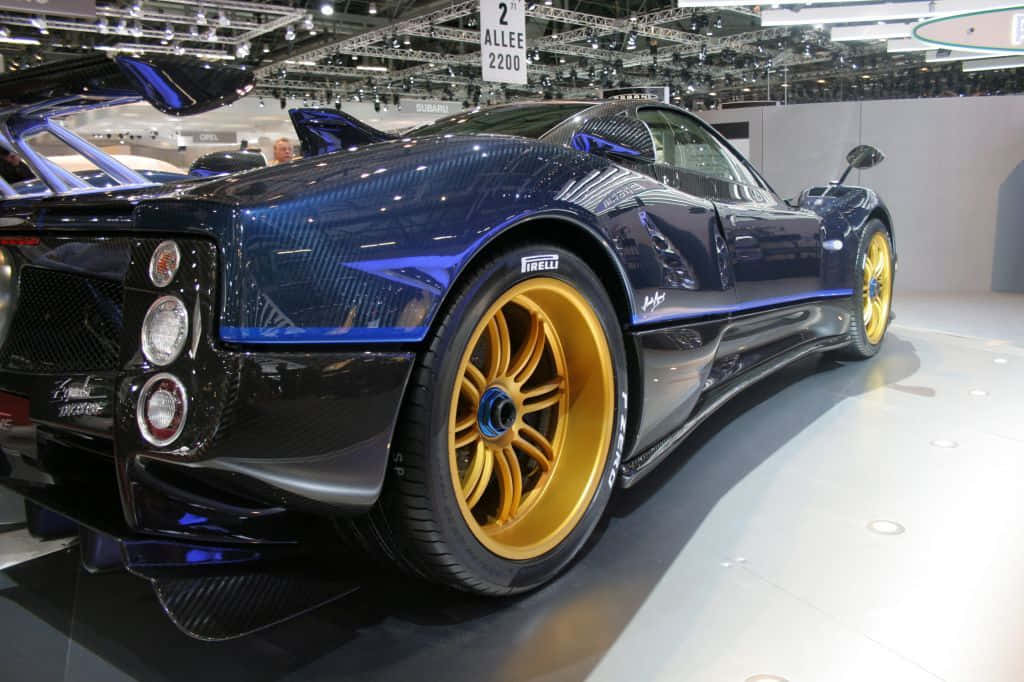 Pagani Zonda Tricolore 桌布 壁紙 — 一輛光澤藍色Pagani Zonda跑車搭配金色輪圈，在明亮燈光下的車展中展出。