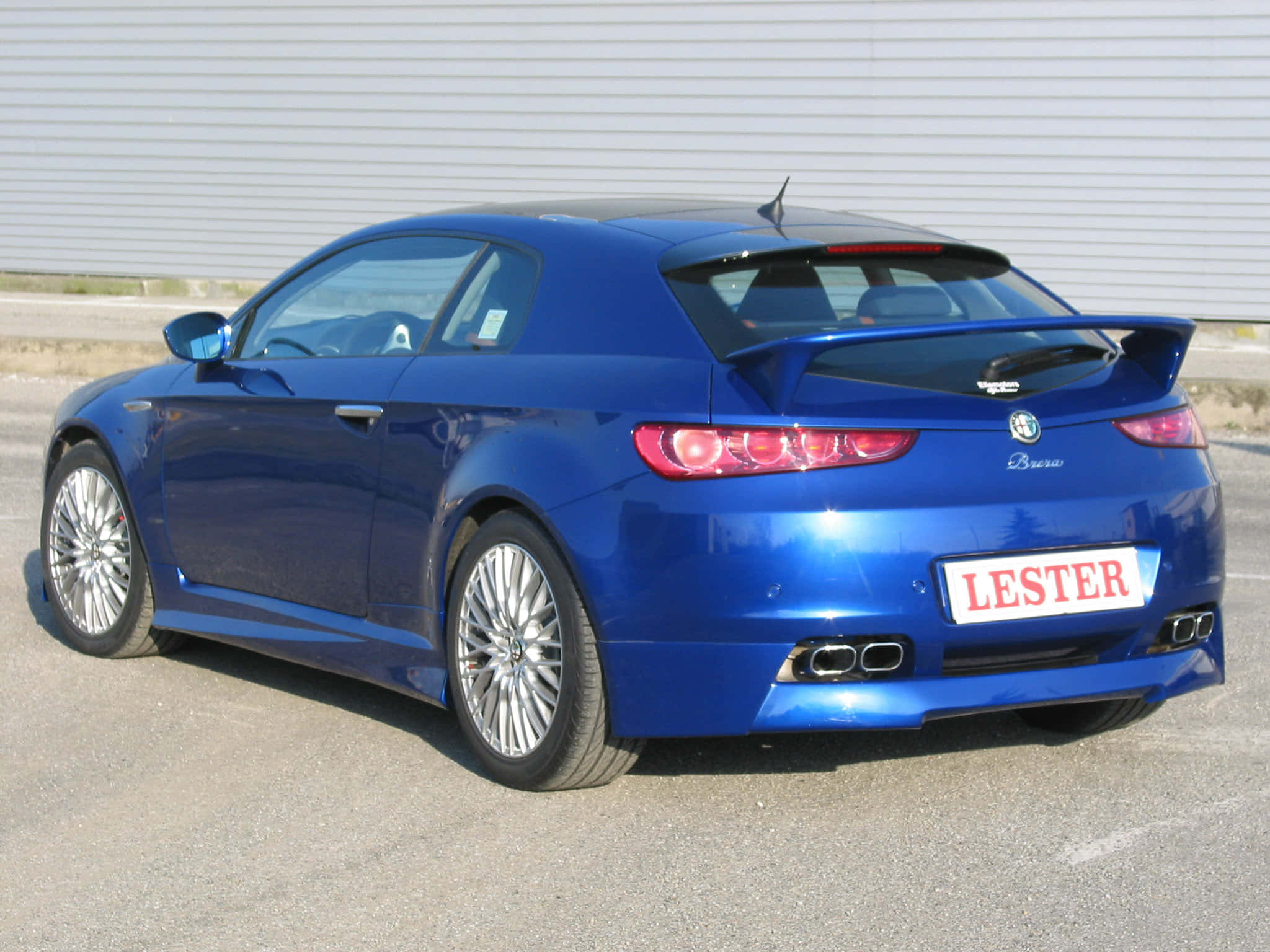 Alfa Romeo Brera 桌布 壁紙 — 一輛光澤藍色的愛快羅密歐 Brera 跑車停在瀝青路上，後面有白色波紋牆。