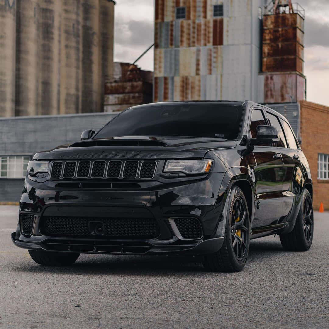 Jeep Trackhawk 桌布 壁紙 — 一輛光澤黑色Dodge Durango SRT停在柏油路上，背景是生鏽的工業筒倉，天空多雲。