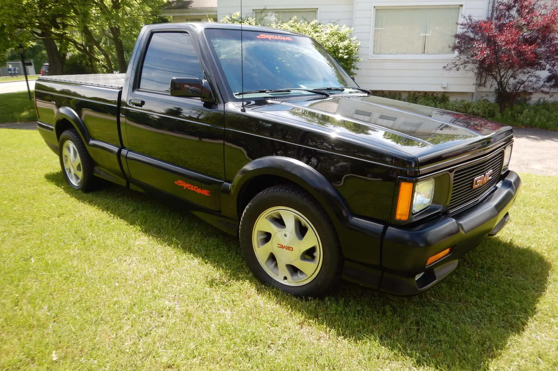 Gmc Syclone 桌布 壁紙 — 一輛光澤黑色GMC Syclone皮卡車配金色輪圈，停放在屋前陽光明媚的綠色草坪上。