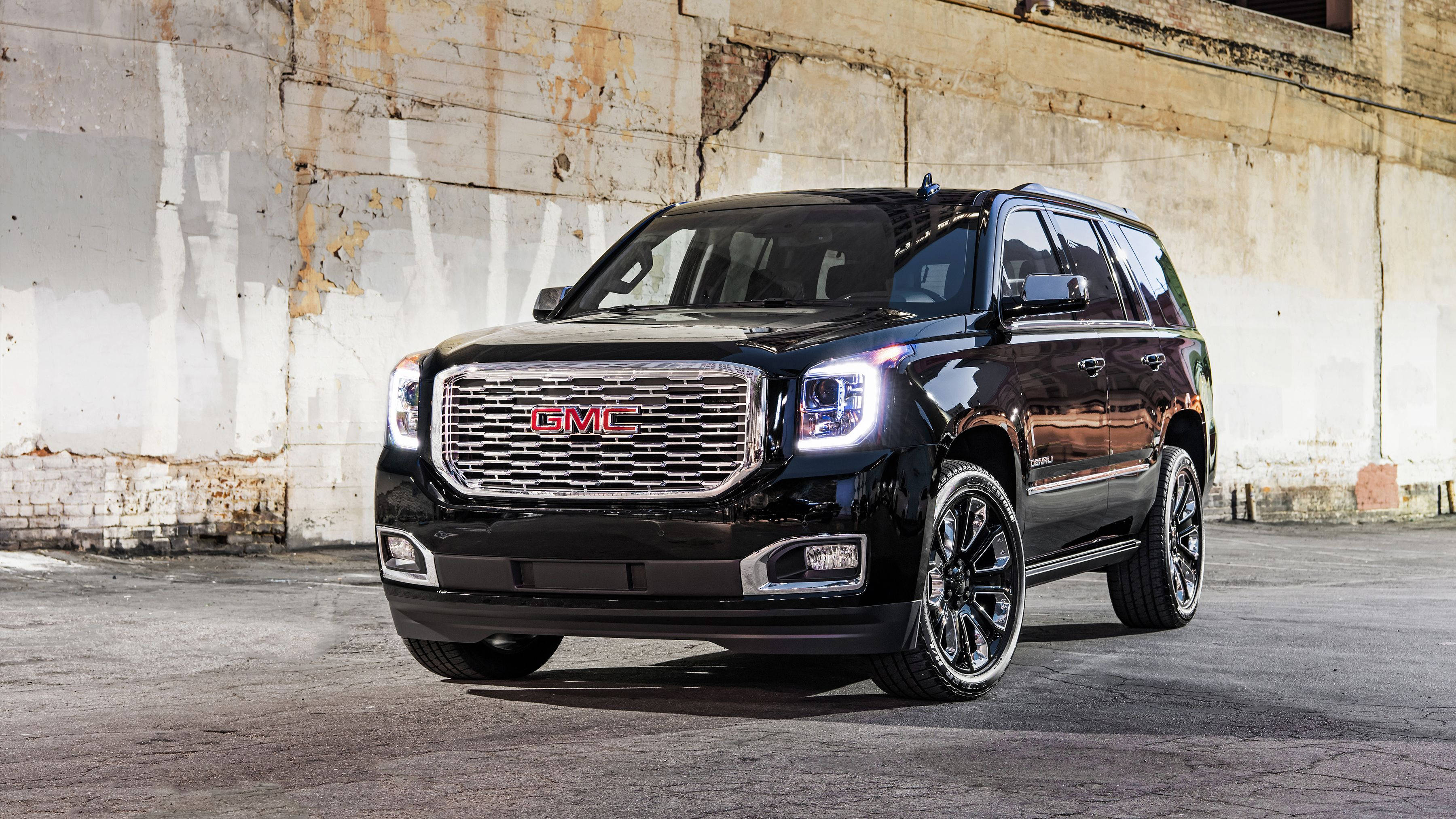 Gmc 桌布 壁紙 — 一輛光澤黑色GMC Yukon SUV，帶有鍍鉻飾邊和定制輪圈，大膽地停在風化混凝土牆前。
