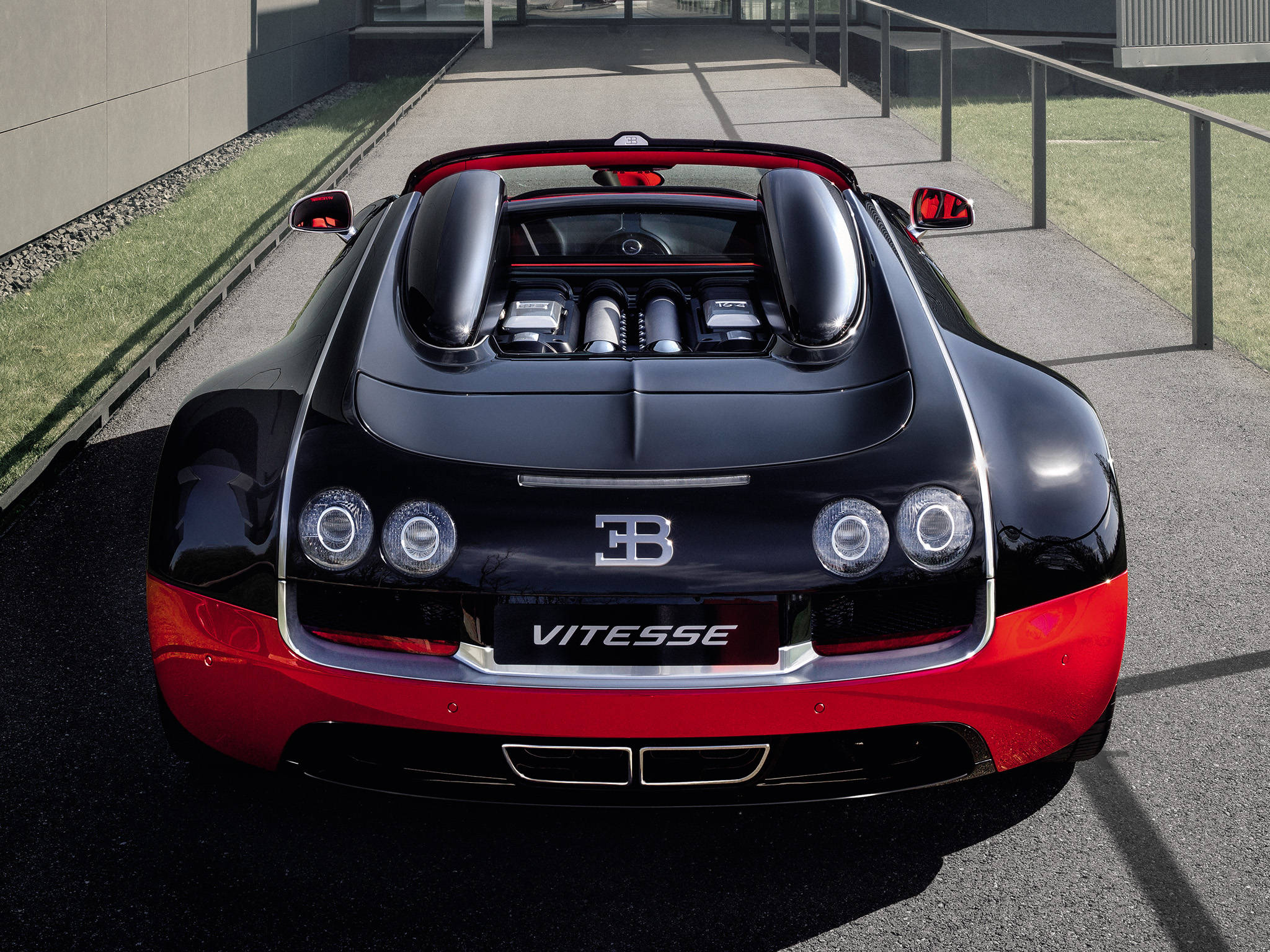 bugatti iPhone 桌布 壁紙 — 一輛光澤黑色和紅色的Bugatti Vitesse超級跑車從後方觀看，露出引擎和四頭燈，停在鋪砌的車道上。