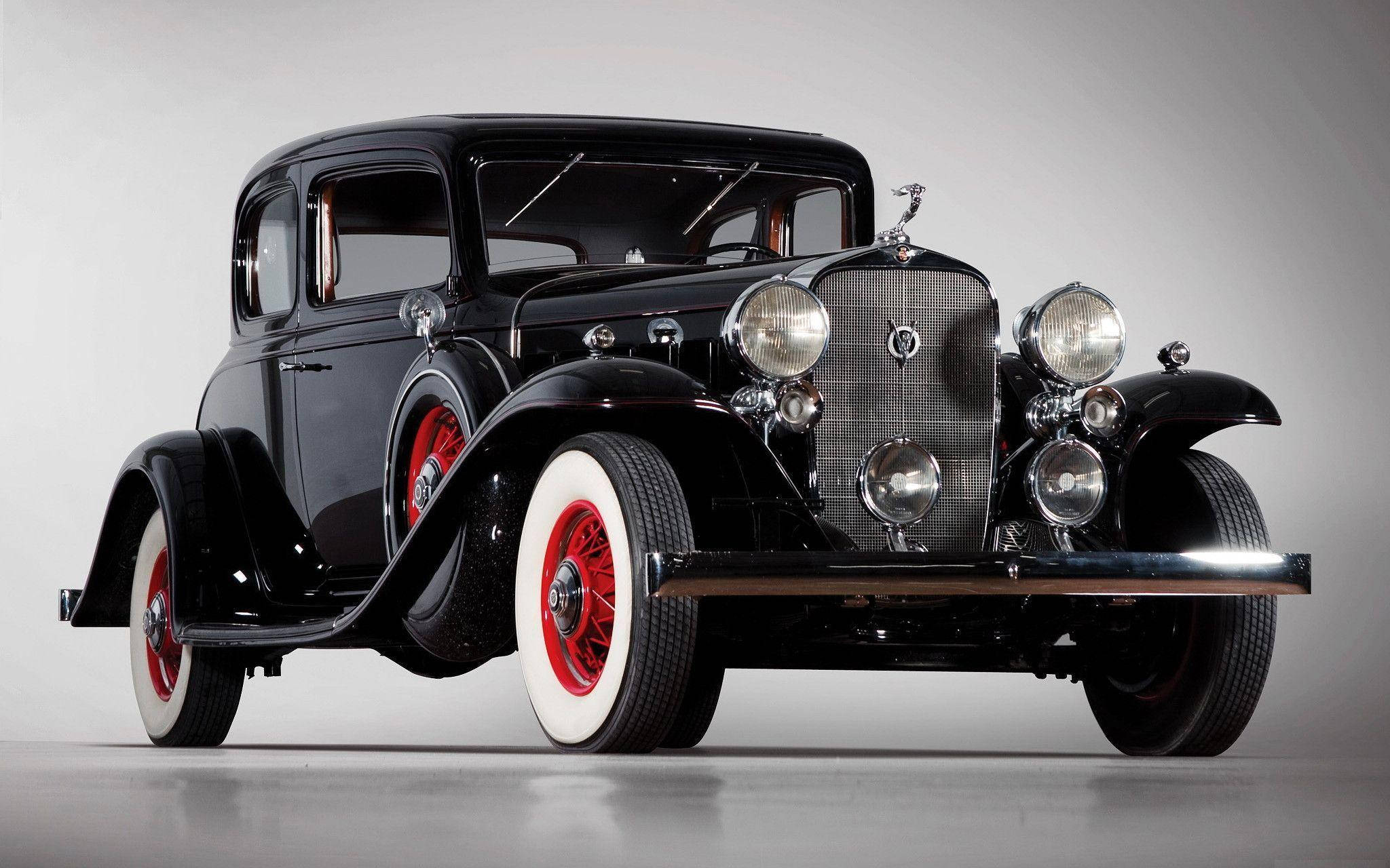 Cadillac 桌布 壁紙 — 一輛光澤黑色復古車，配備紅色鋼絲輪圈和白色側壁輪胎，在中性攝影棚背景前擺好姿勢。