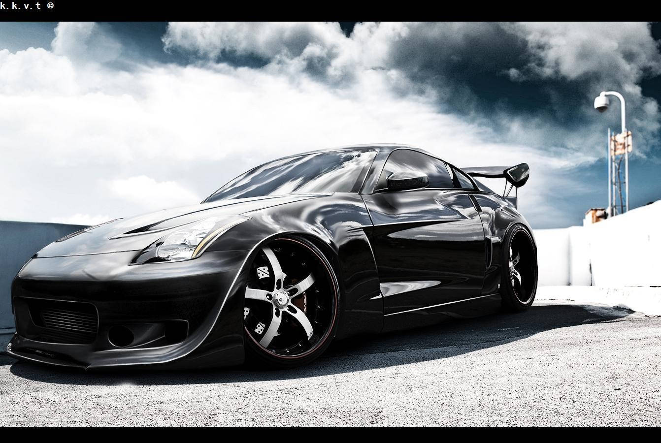 Nissan 350z 桌布 壁紙 — 一輛光澤黑色改裝跑車，配備寬體套件和大輪圈，停在戲劇性多雲天空下的瀝青路面上。
