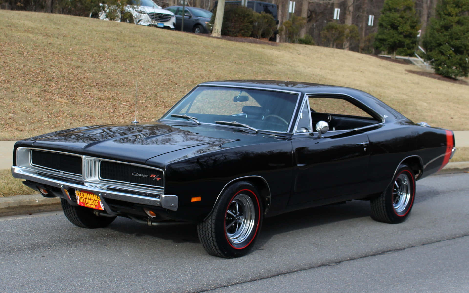 1969 年道奇 Charger 桌布 壁紙 — 一輛光澤黑色經典肌肉車配紅線輪胎，停泊在郊區街道旁，旁邊有草坡。