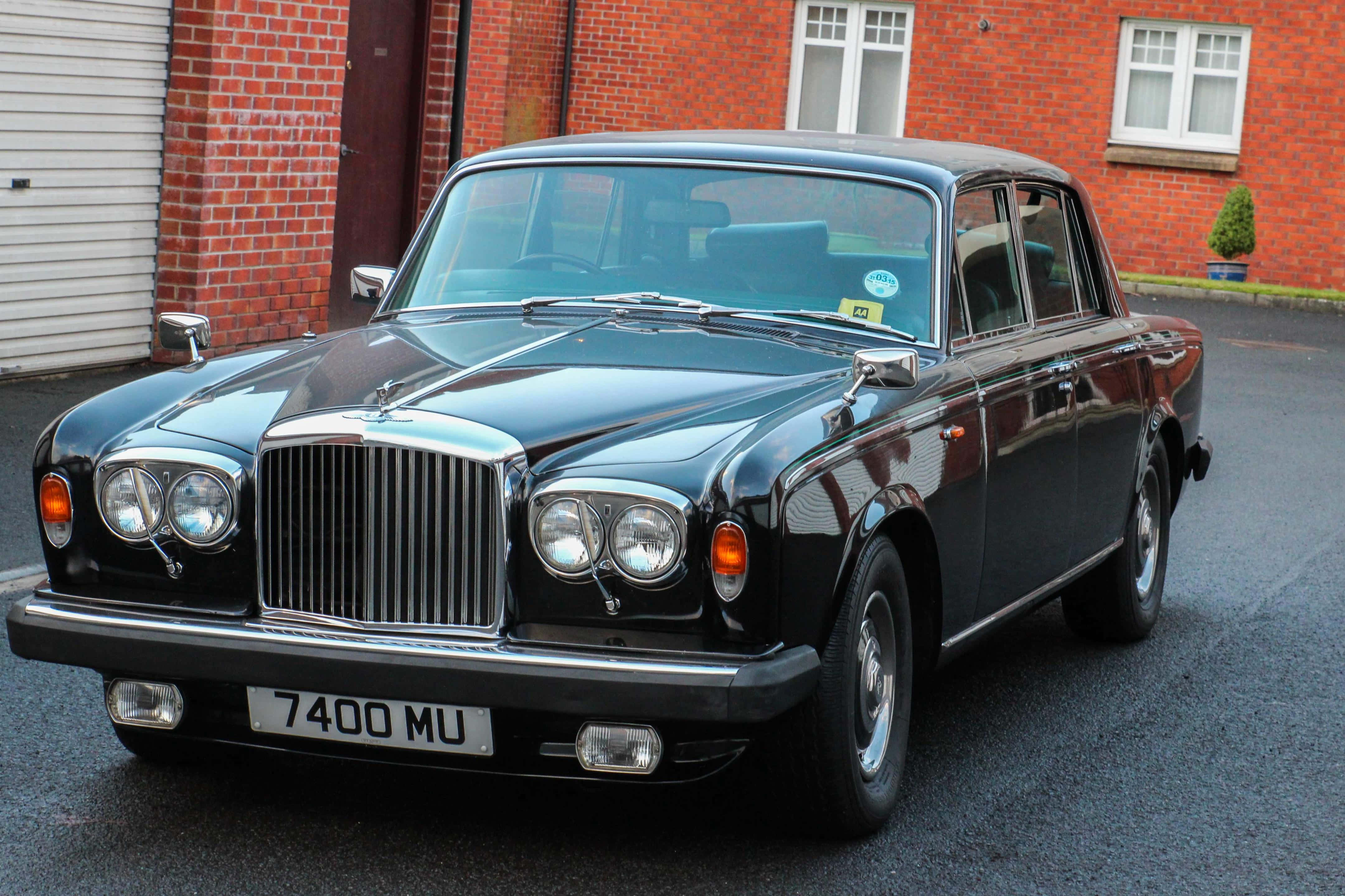 Bentley T2 桌布 壁紙 — 一輛光澤黑色經典賓利轎車停放在紅磚建築前的柏油路上，建築物有白色窗戶。