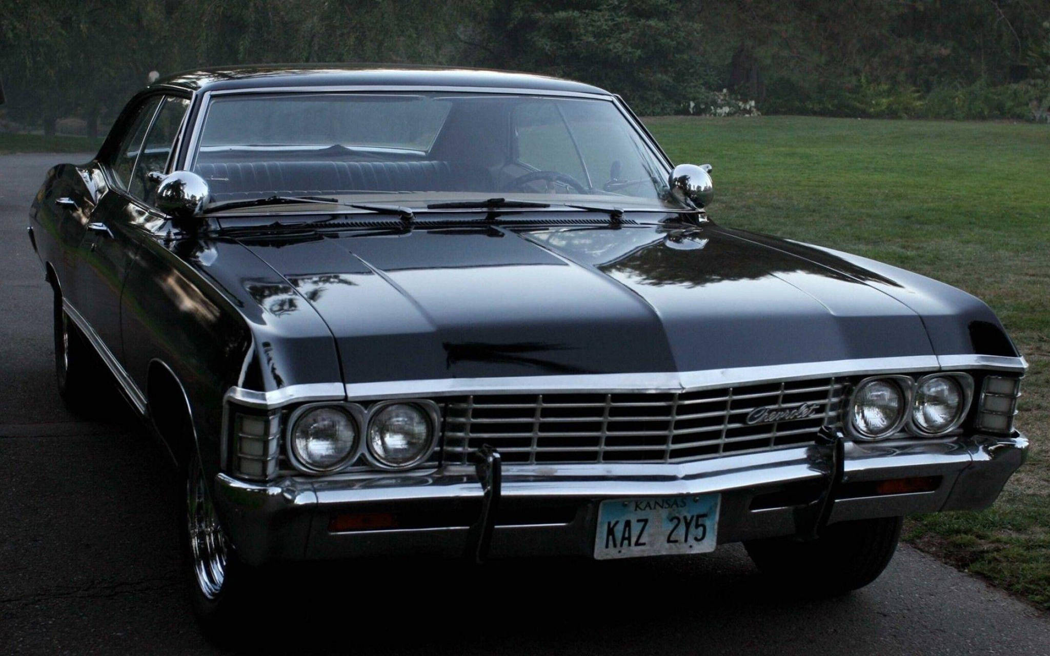 chevrolet impala 1967 桌布 壁紙 — 一輛光澤黑色經典雪佛蘭，帶有鍍鉻裝飾，停在草地旁的柏油路上。