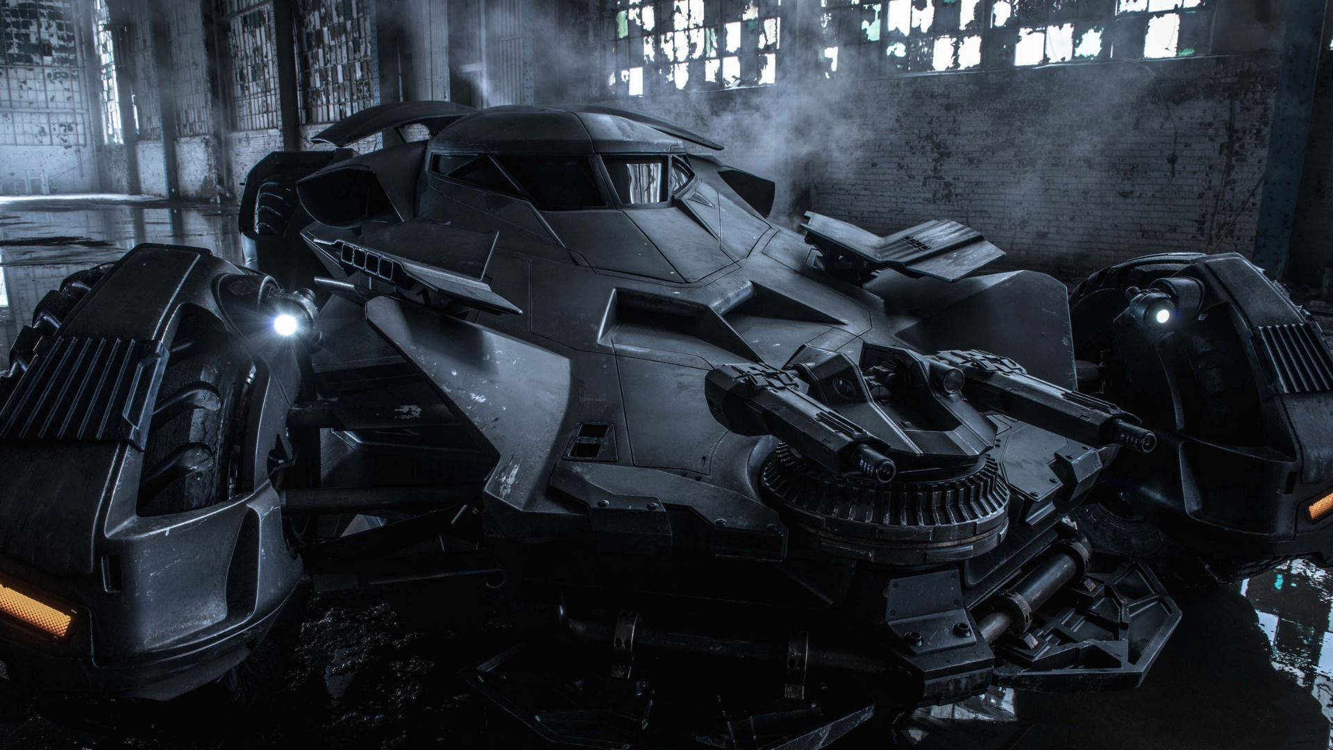 Batmobile 桌布 壁紙 — 一輛具威脅性的黑色裝甲蝙蝠車停放在一個煙霧瀰漫、窗戶破損、水坑映照其銳利線條的廢棄倉庫中。