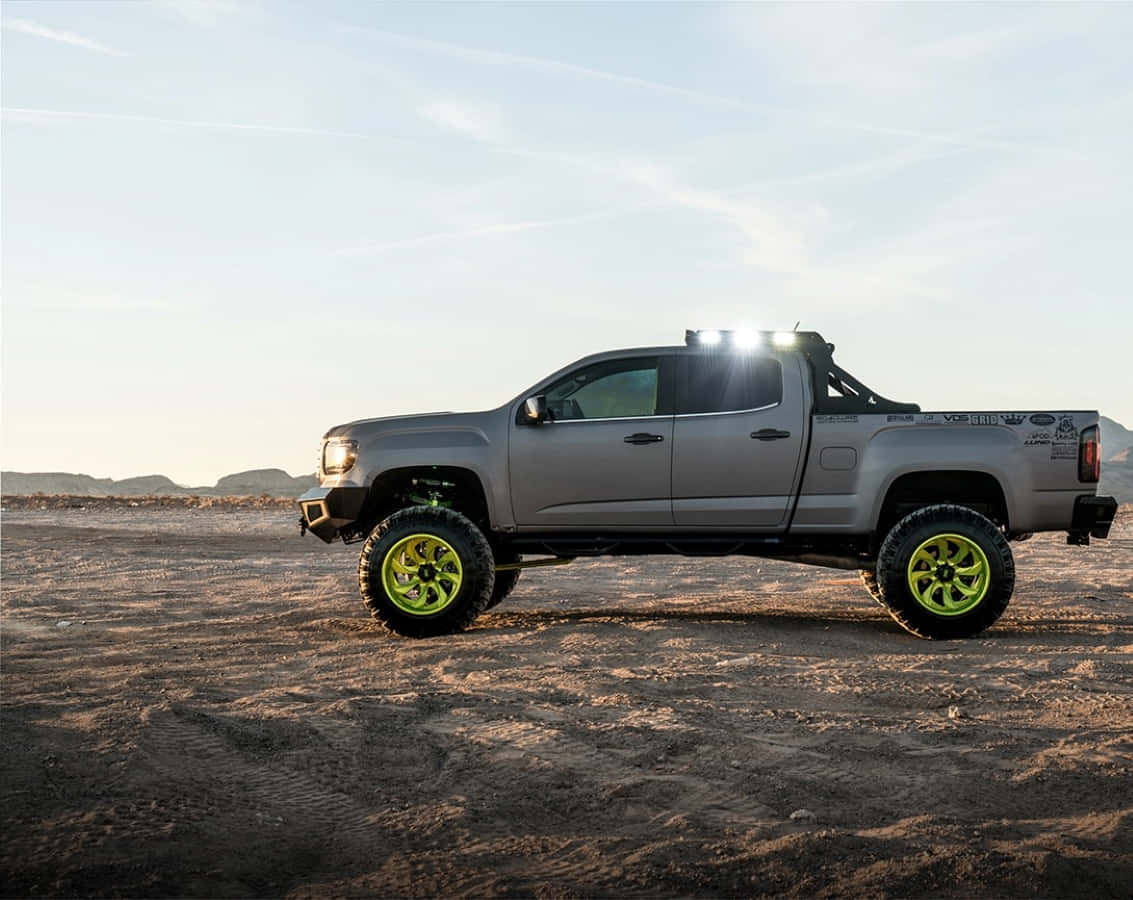 Gmc Canyon 桌布 壁紙 — 一輛升高的灰色皮卡車搭配螢光綠色車輪，在晴朗的天空下矗立於陽光普照的沙漠地形上。
