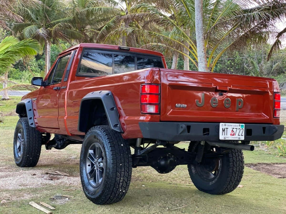 Jeep Comanche 桌布 壁紙 — 一輛升高的紅色Jeep Wrangler，配有大輪胎，停泊在熱帶環境中的棕櫚樹下草地上。