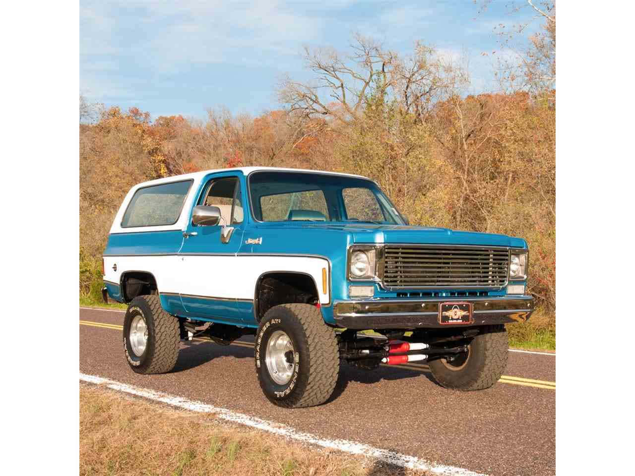 Gmc Jimmy 桌布 壁紙 — 一輛升高的藍白色Jeep Cherokee在晴朗天空下行駛在鋪砌道路上，穿過秋天的樹林。