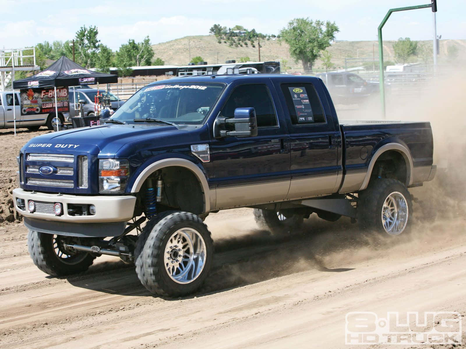 Jacked Up Trucks 桌布 壁紙 — 一輛升高的藍色福特Super Duty卡車在明亮的日光下在泥土賽道上高速行駛，揚起灰塵。