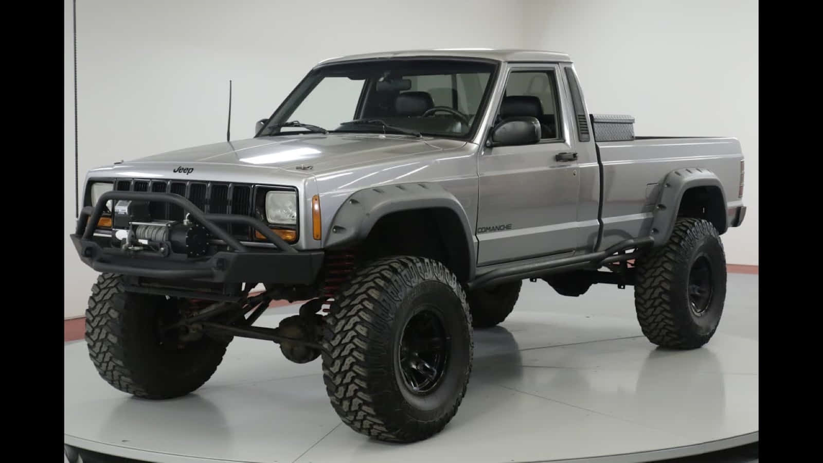 Jeep Comanche 桌布 壁紙 — 一輛升高的銀色Jeep Cherokee XJ，配備超大輪胎和黑色保險桿，站在白色的工作室轉盤上。