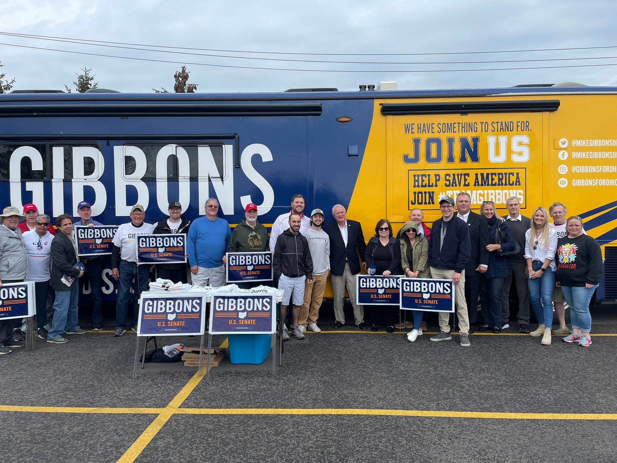 Politics 桌布 壁紙 — 一輛印有「GIBBONS U.S. SENATE」標誌的競選巴士停在停車場，一群支持者在陰天舉著相應的標語牌。