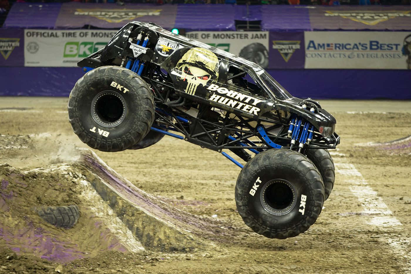 Monster Truck 桌布 壁紙 — 一輛名為「Bounty Hunter」的黑色怪獸卡車在室內場地的泥土坡道上空飛翔，這是Monster Jam活動中的一幕。