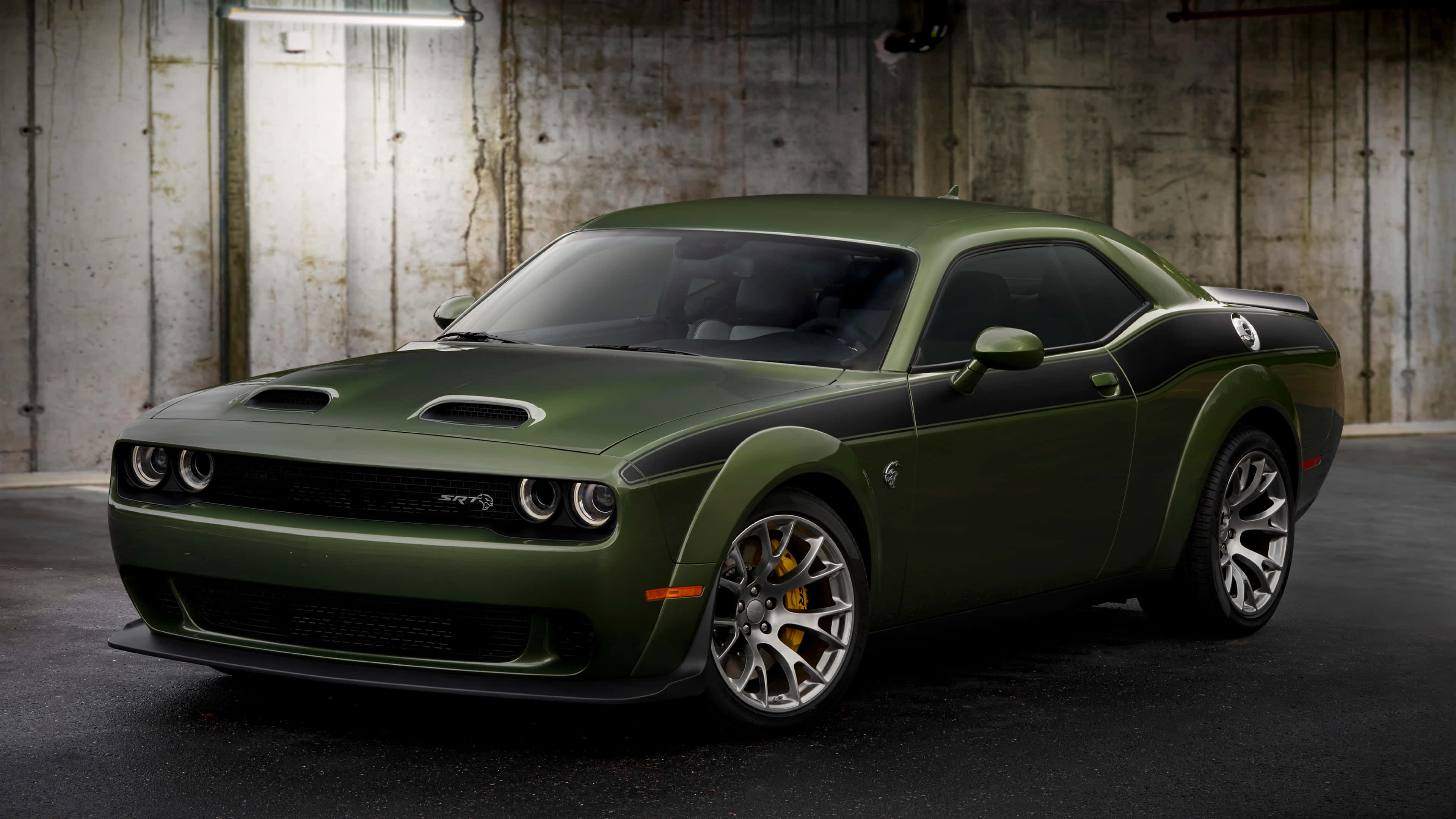 汽車 4K 桌布 壁紙 — 一輛啞光橄欖綠色的Dodge Challenger SRT Hellcat，帶有黑色賽車條紋，停放在燈光昏暗的混凝土車庫中。
