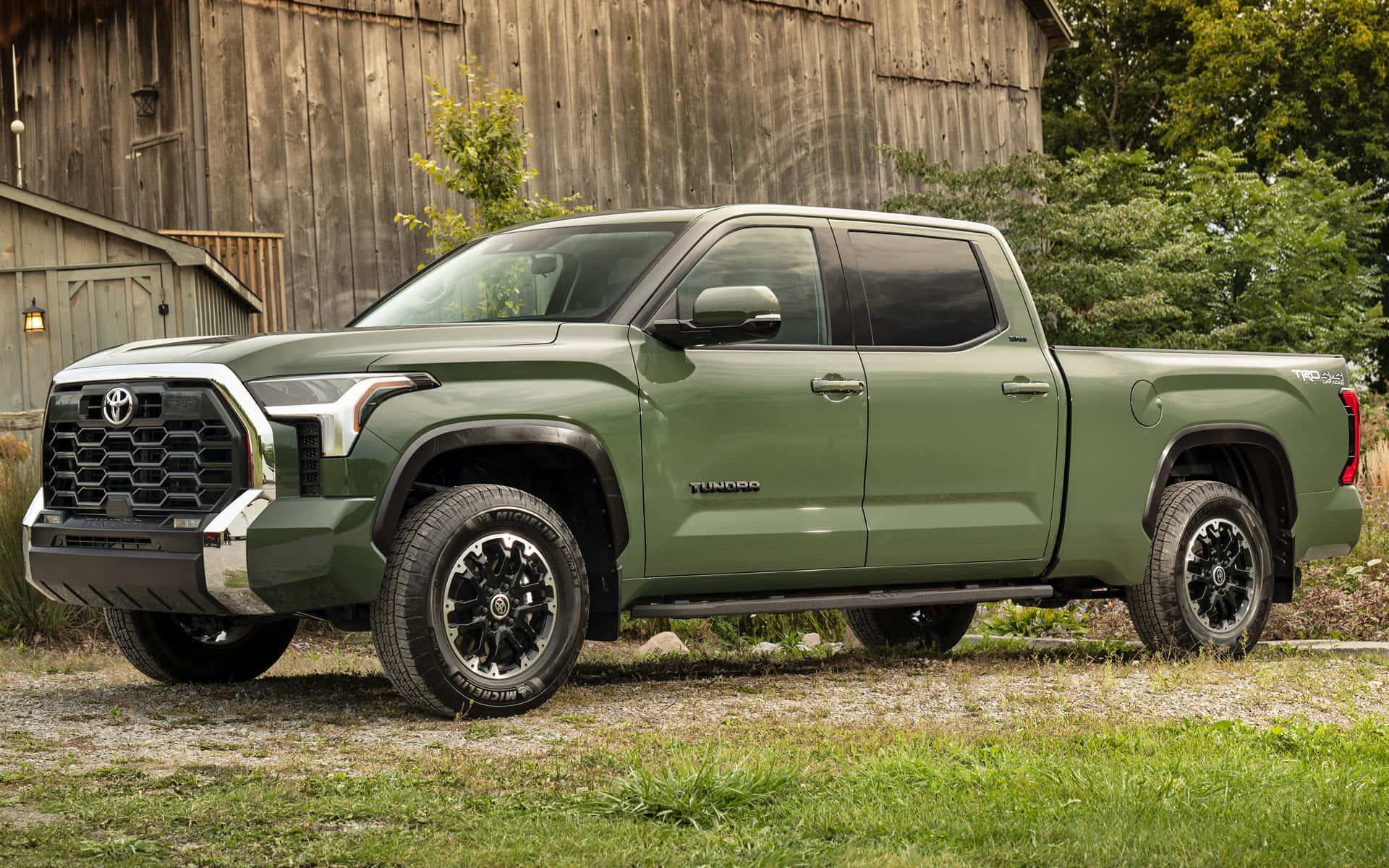 Toyota 桌布 壁紙 — 一輛啞光橄欖綠色的豐田Tundra皮卡車停在碎石路上，旁邊是一座風化的木製穀倉，背景是茂密的綠植。