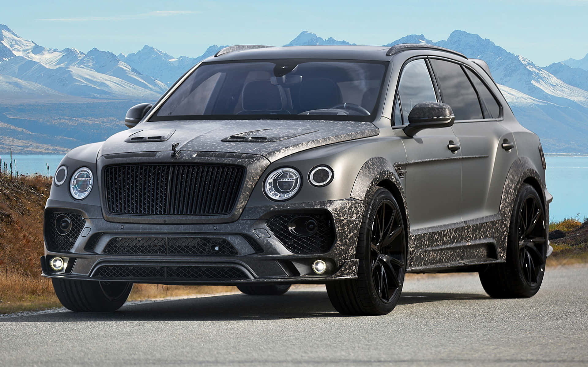 Bentley Bentayga 桌布 壁紙 — 一輛啞光灰色 Bentley Bentayga SUV 帶有迷彩細節，停放在道路上，背景是雪山和湖泊。