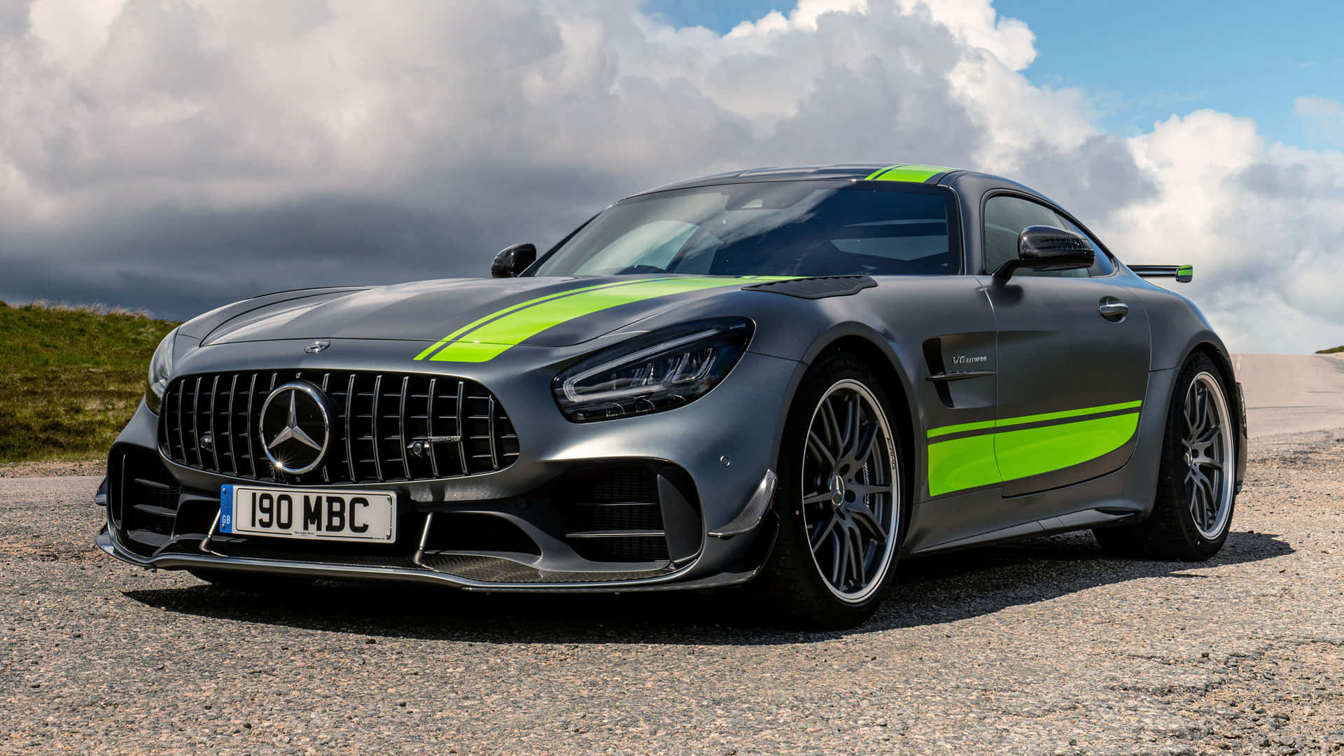 汽車 桌布 壁紙 — 一輛啞光灰色 Mercedes-AMG GT R 跑車，帶有螢光綠色條紋，停泊在陰天天空下的碎石路上。