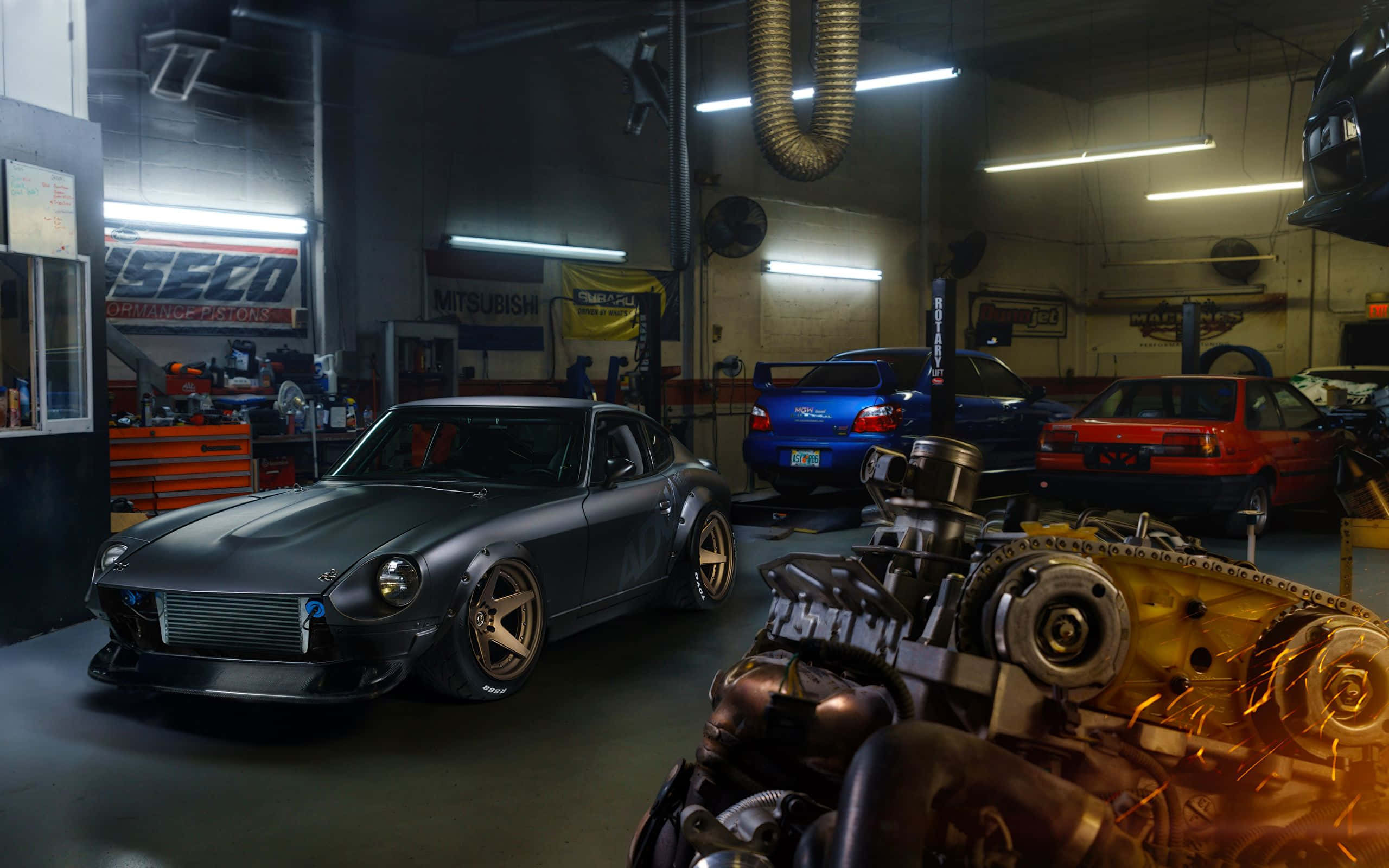 Garage 桌布 壁紙 — 一輛啞光灰色改裝的Datsun 240Z停放在昏暗的車庫中，周圍有其他汽車和引擎零件，在螢光燈下。