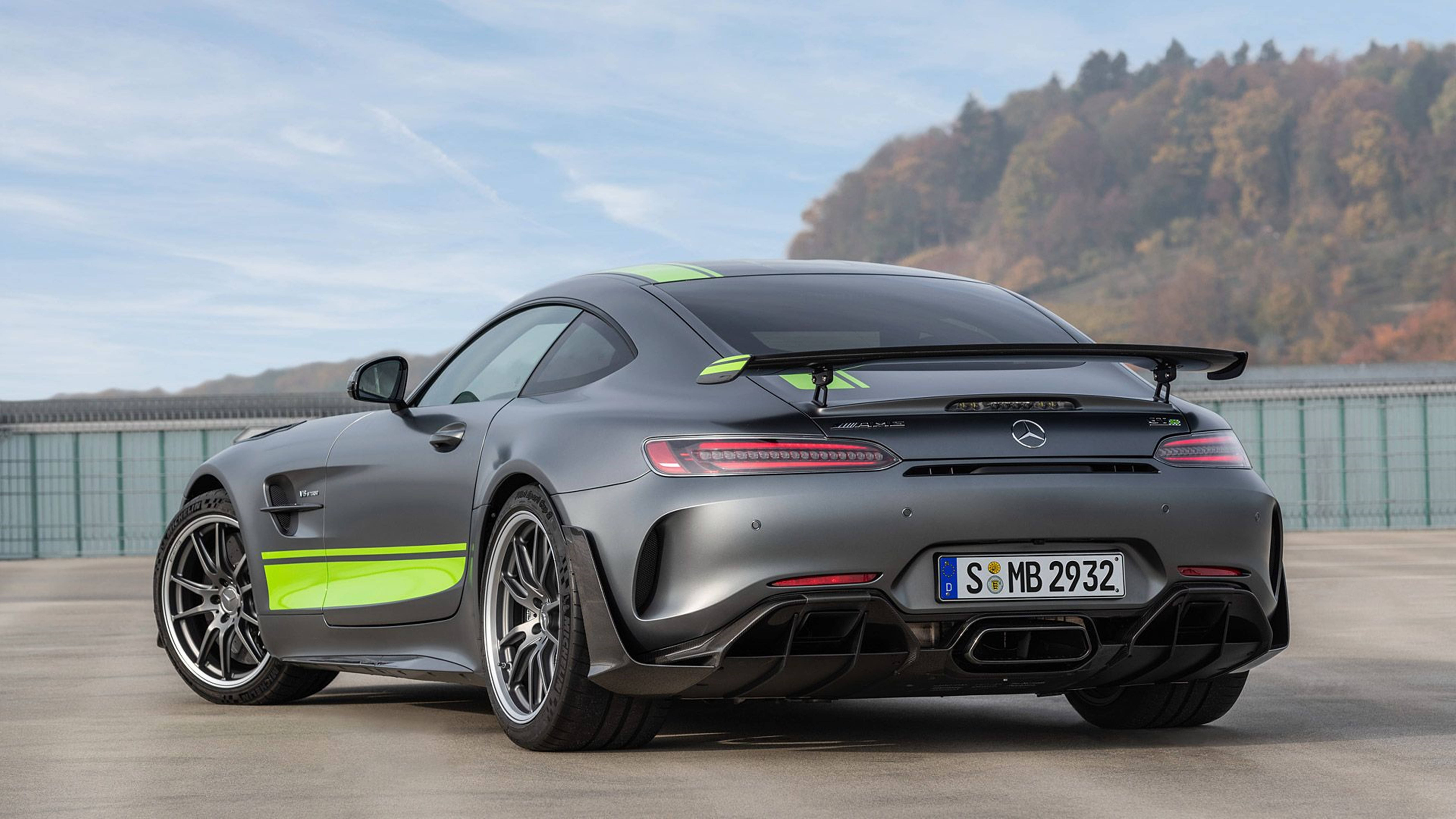 啞光灰色梅賽德斯-AMG GT R 帶有螢光綠色點綴，停放在戶外，靠近樹木繁茂的山丘。 — 4K 奔馳壁紙 壁紙