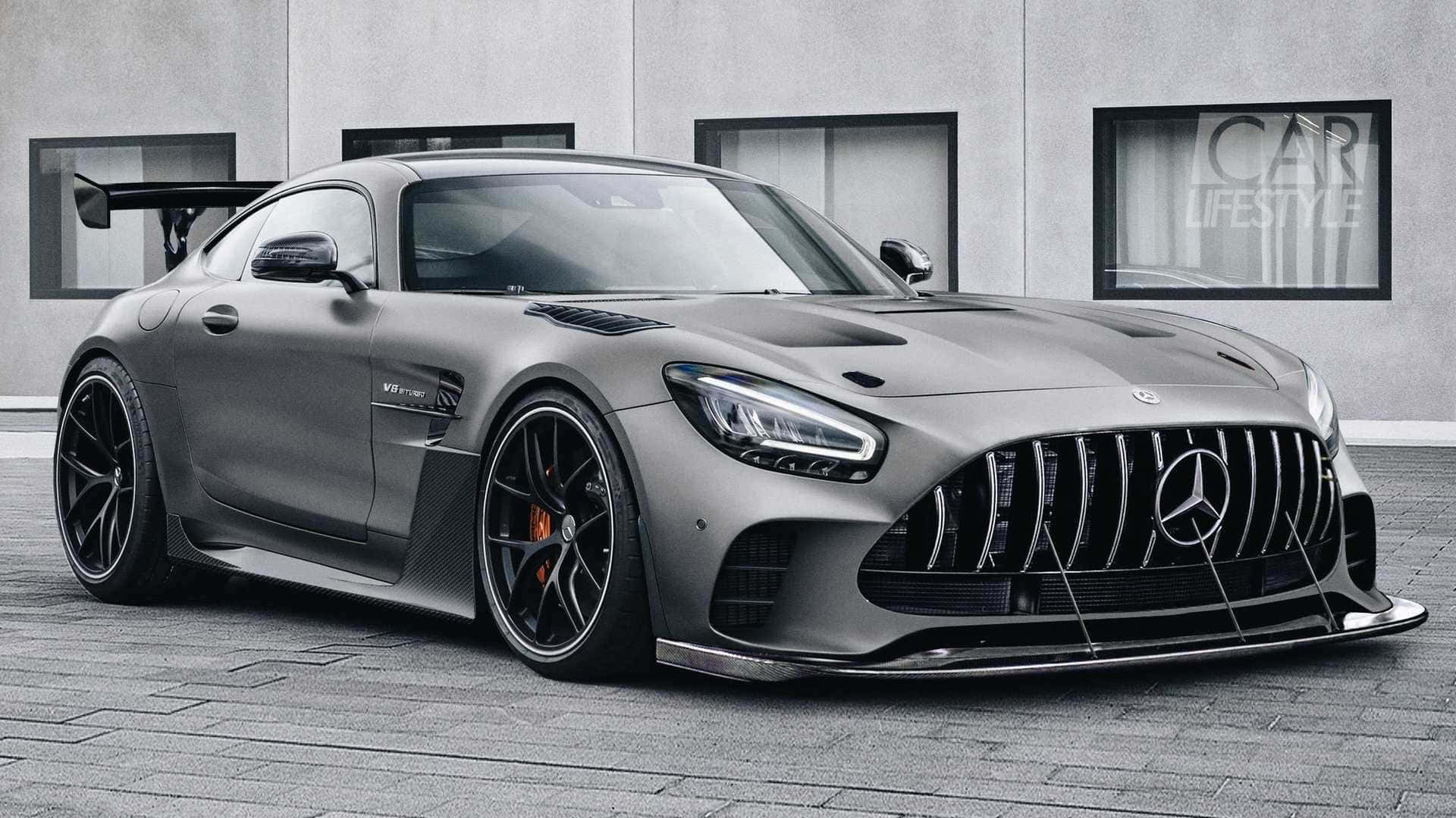 Mercedes Benz Amg Gt 桌布 壁紙 — 一輛啞光灰色的 Mercedes-AMG GT R 跑車，配備黑色輪圈和後擾流板，停放在現代建築物前的瓷磚路面上。