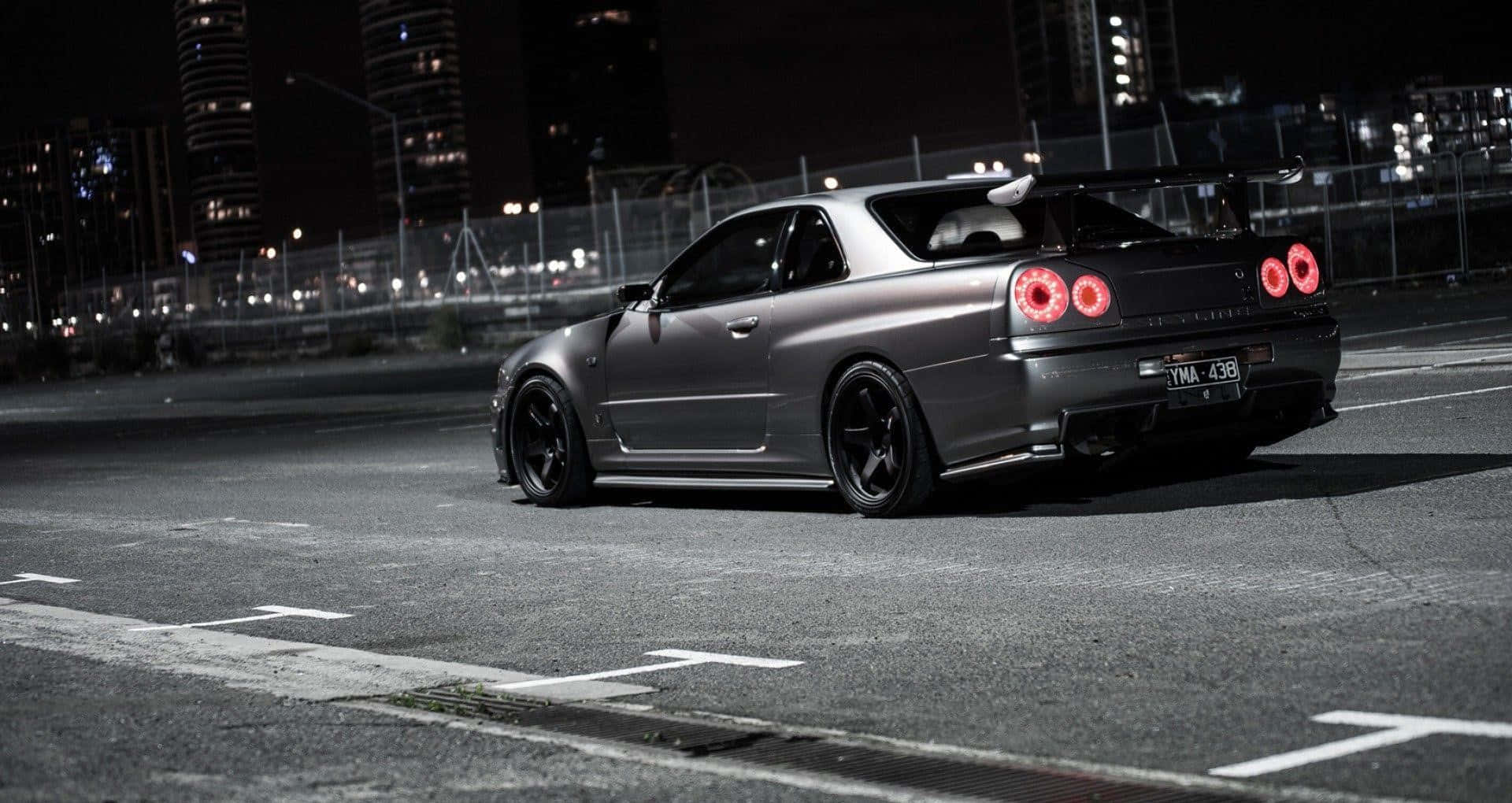 Tuned Car 桌布 壁紙 — 一輛啞光灰色的日產Skyline GT-R，紅色尾燈發光，停在夜晚空無一人的城市街道上。